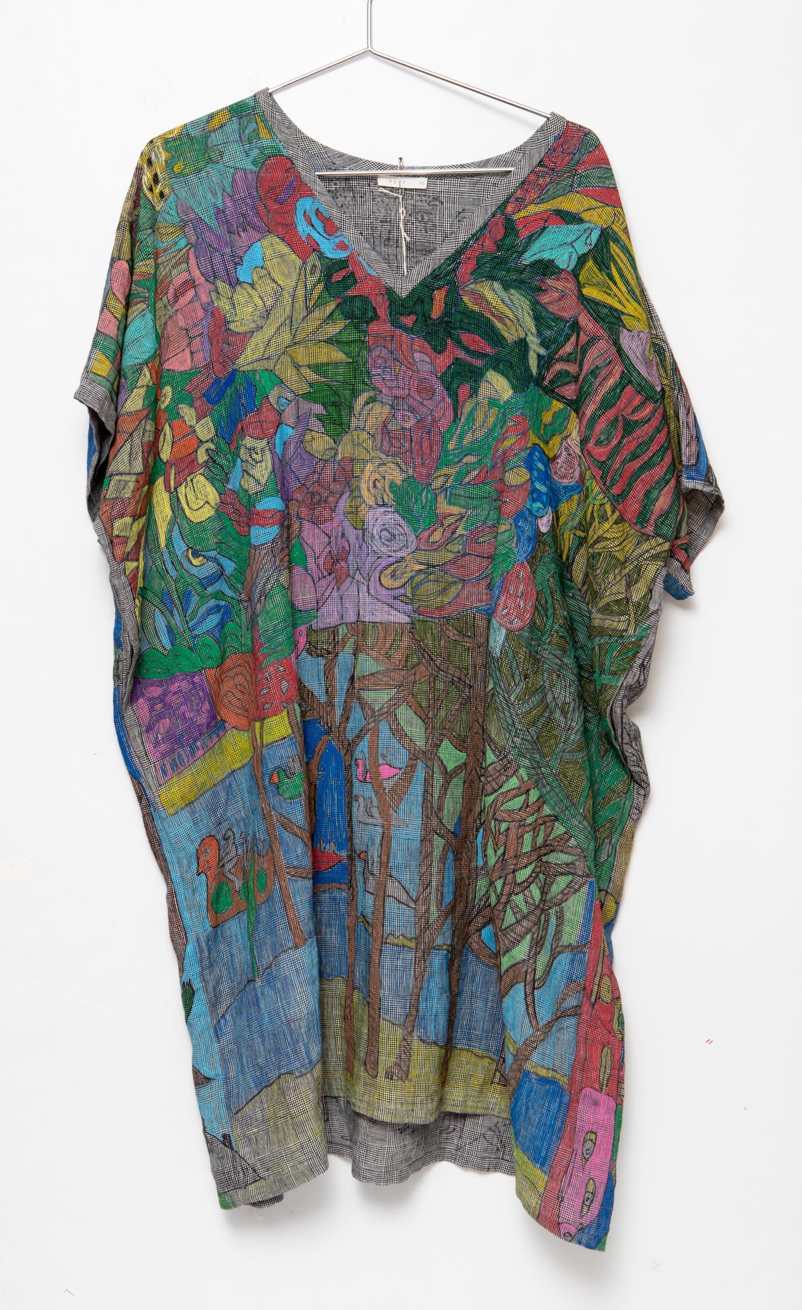 A loose-fitting kaftan garment on a hanger printed with dense, multicolor botanical and figural imagery on gray checked fabric.