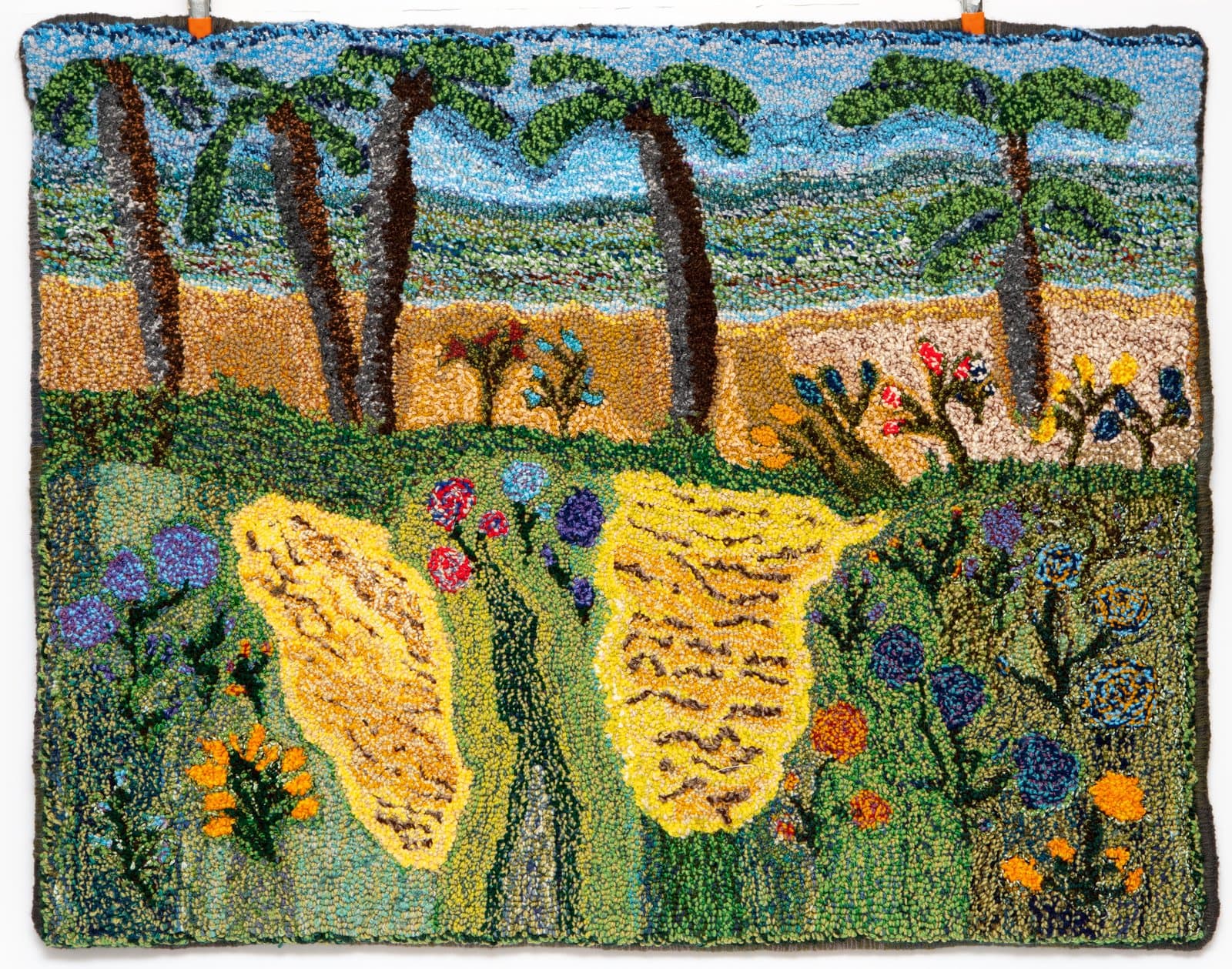 Hooked rug depicting a large yellow butterfly amid wildflowers, with palm trees, sandy terrain, and blue sky beyond.