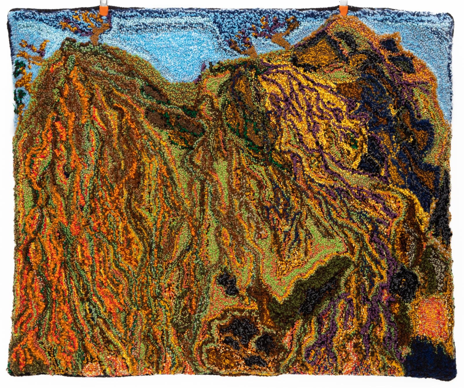 Tufted rug depicting two large mountainous forms in orange, green, and purple beneath a light blue sky.