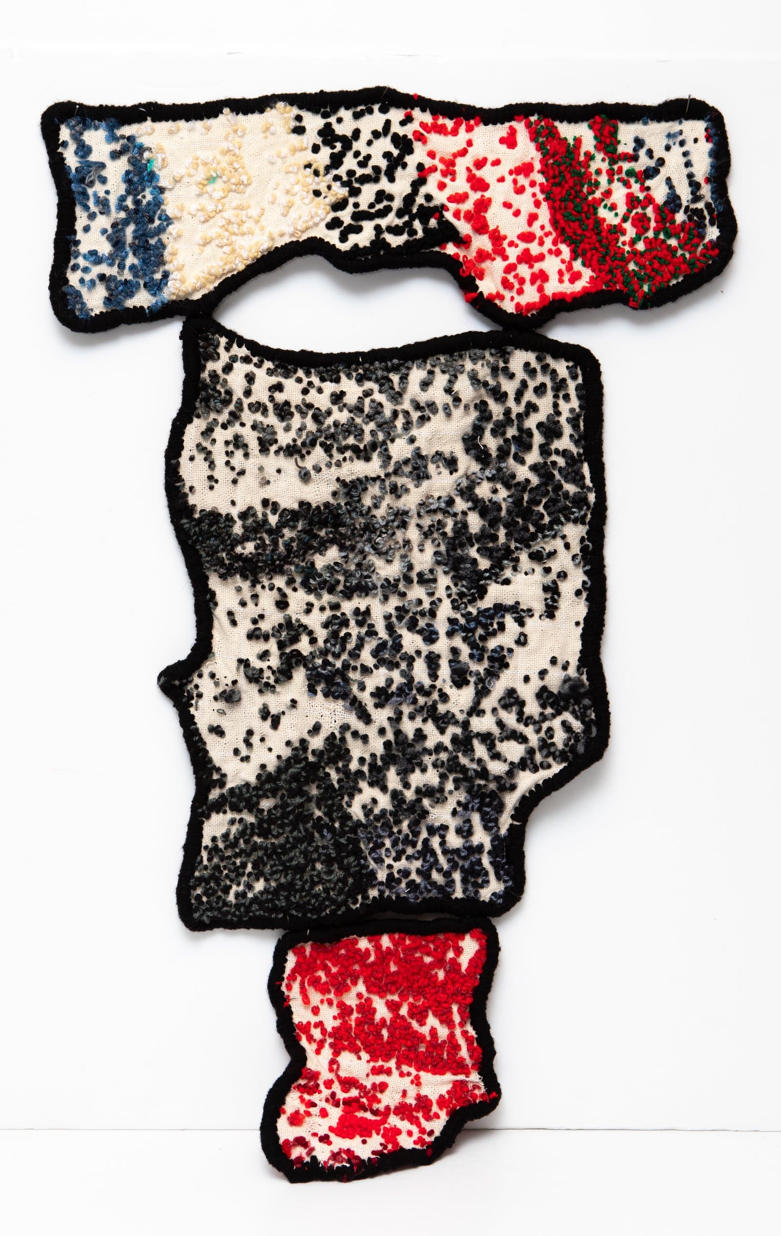 Soft sculpture with three irregular fabric panels edged in black, densely embroidered with black, red, blue, and white knots.