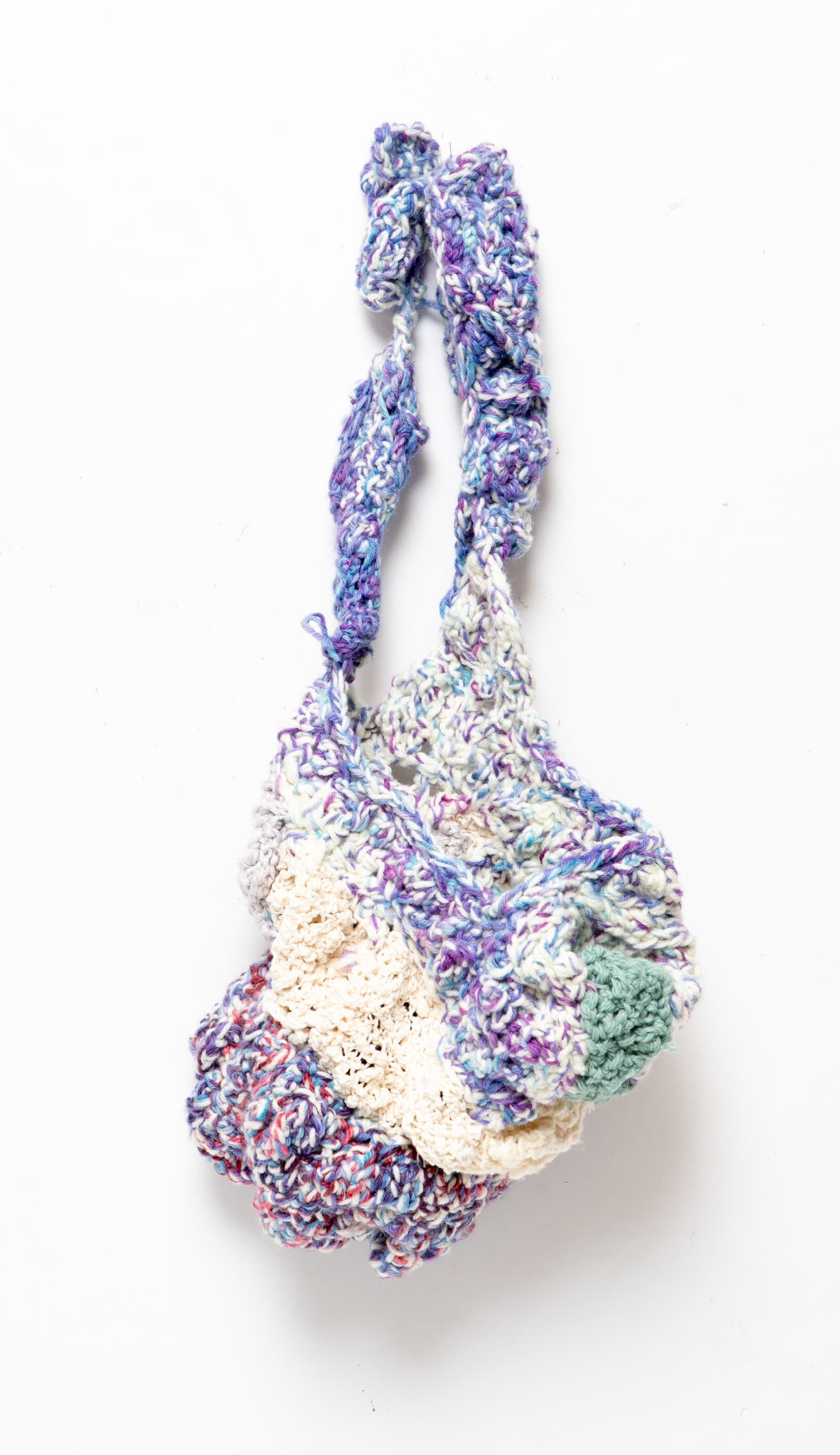 Crocheted textile bag with ruffled body in variegated purple, blue, cream, and teal yarn, suspended by a looped handle.