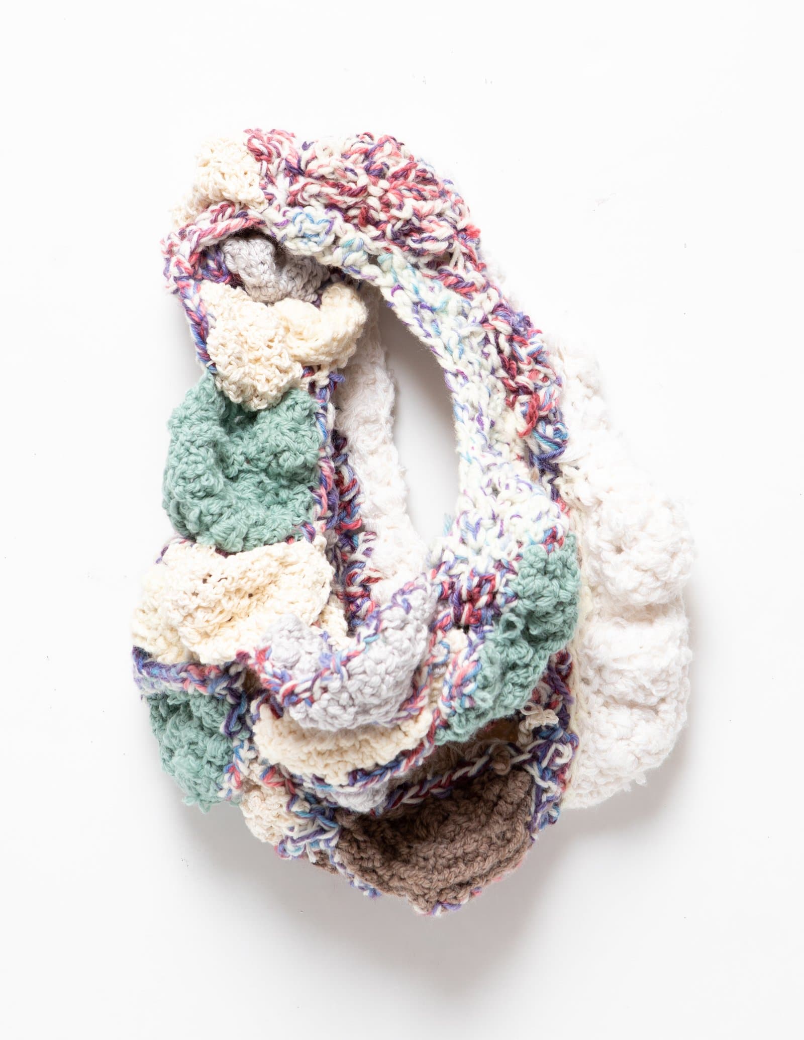 Sculptural crocheted textile artwork mounted on wall, featuring looping forms in cream, sage green, taupe, and multicolor yarn.