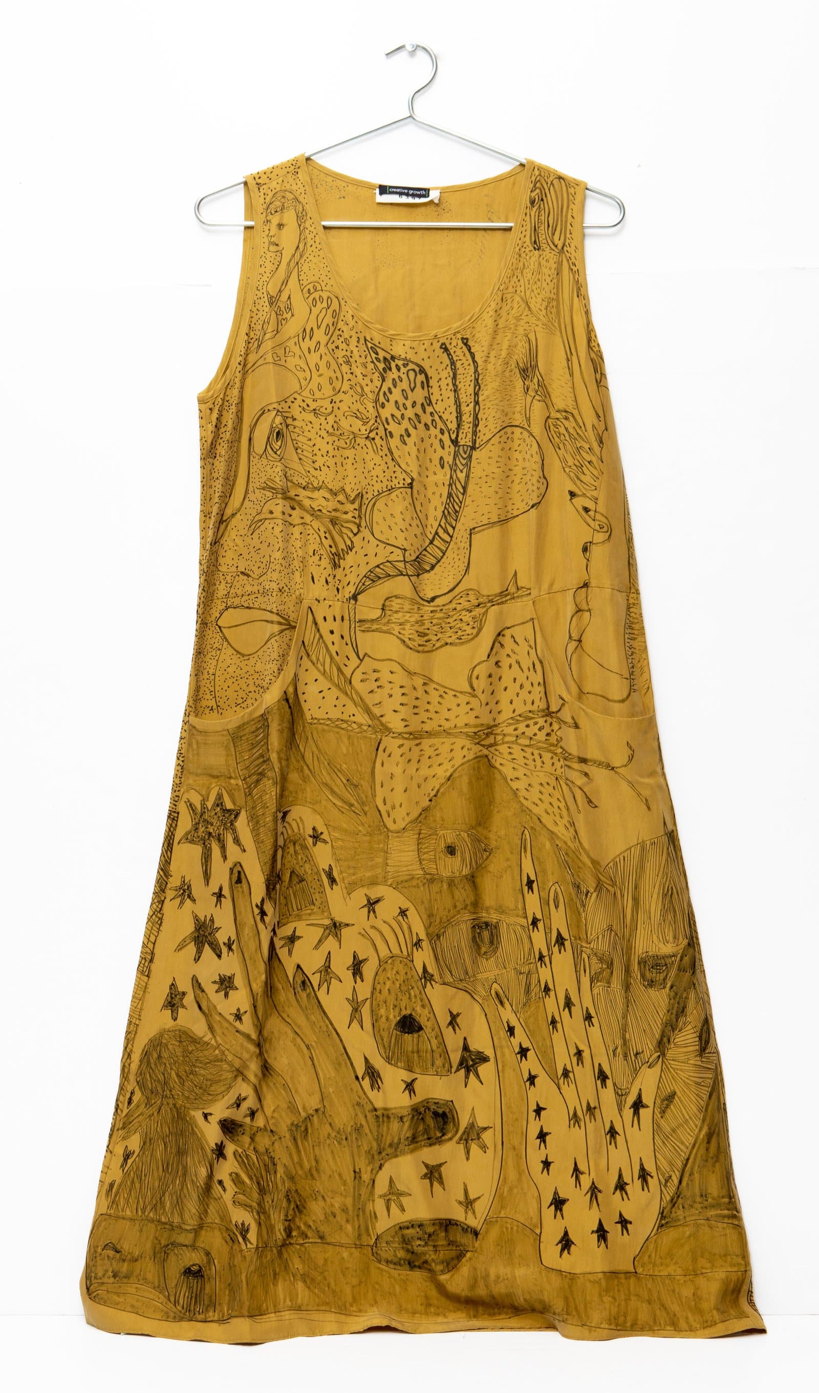 Sleeveless A-line dress in mustard yellow cotton with dense black line drawings of figures, birds, and stars across the fabric.