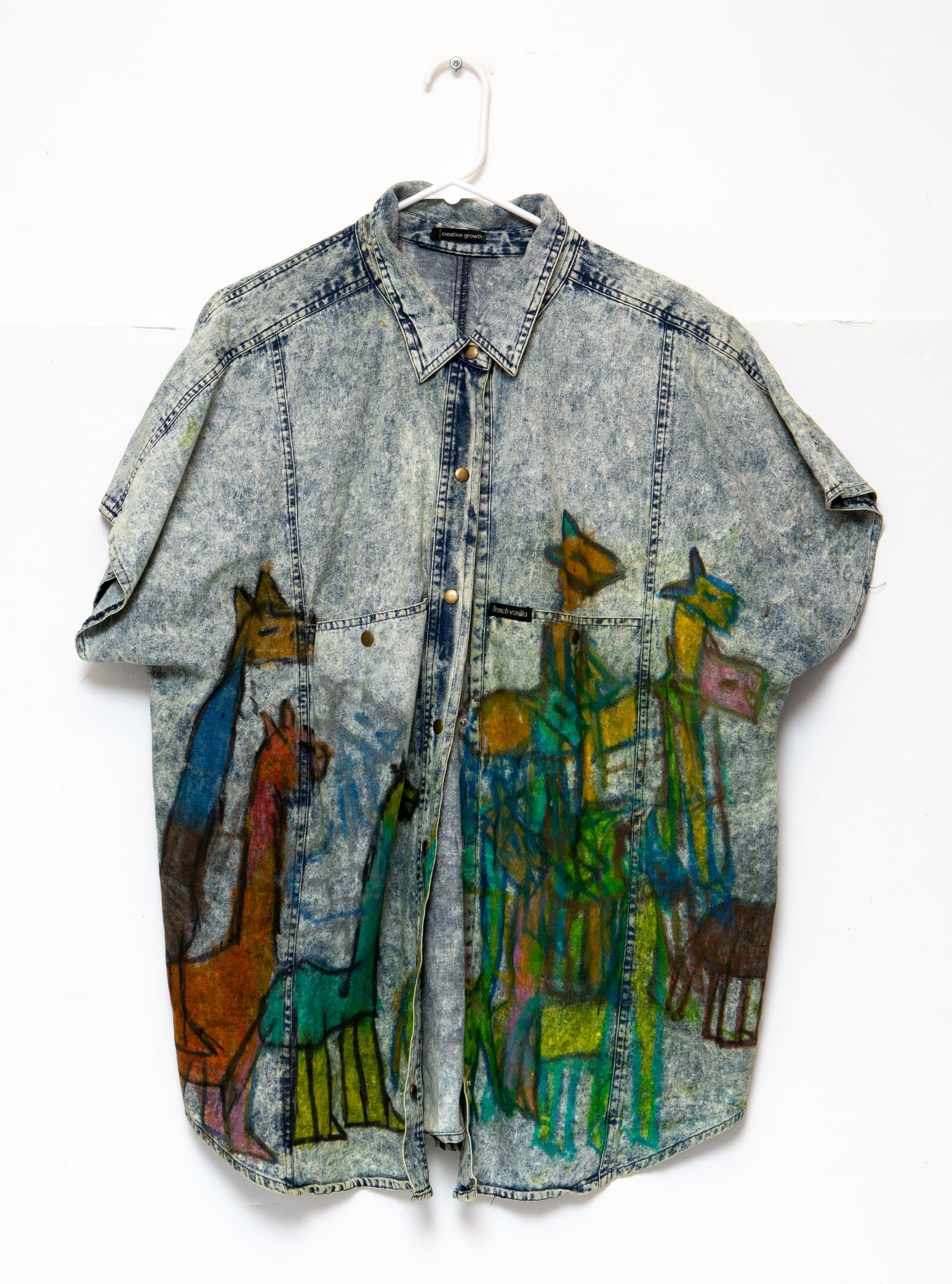 Acid-wash denim shirt displayed on hanger, decorated with hand-drawn figures of animals and people in multicolor marker.
