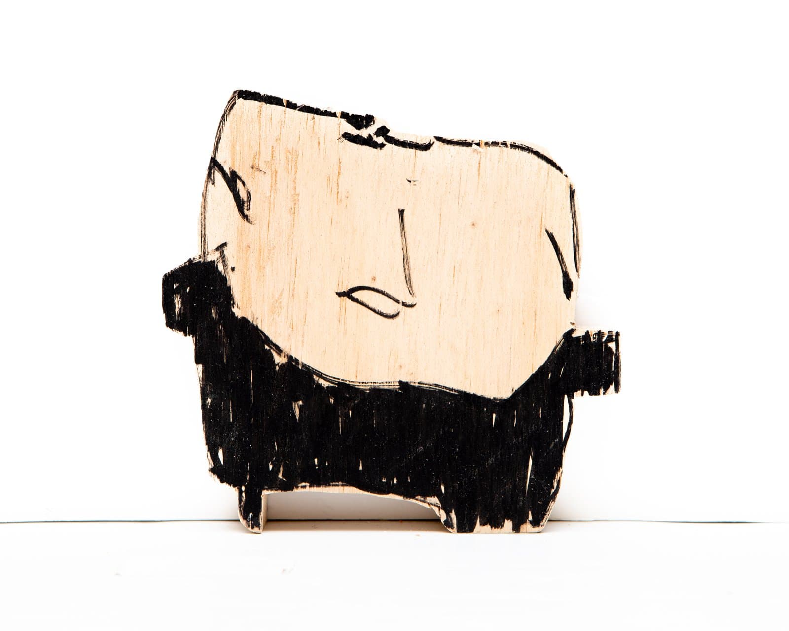 Small wood cutout sculpture of a simplified face with black acrylic marker, showing pale wood grain skin and dark hair/beard.