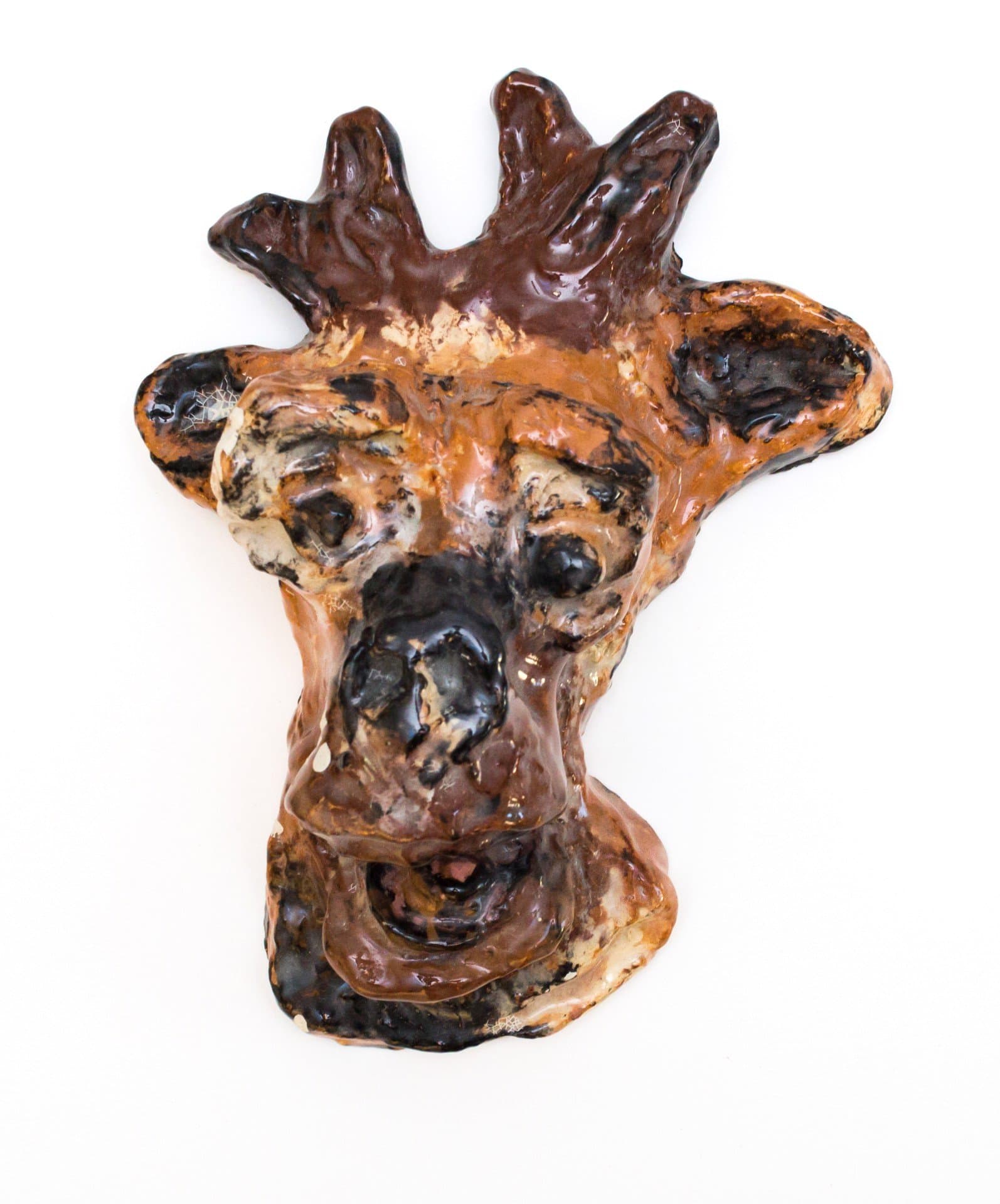 Ceramic sculpture of a distorted giraffe head with glossy brown and orange glazes on white background