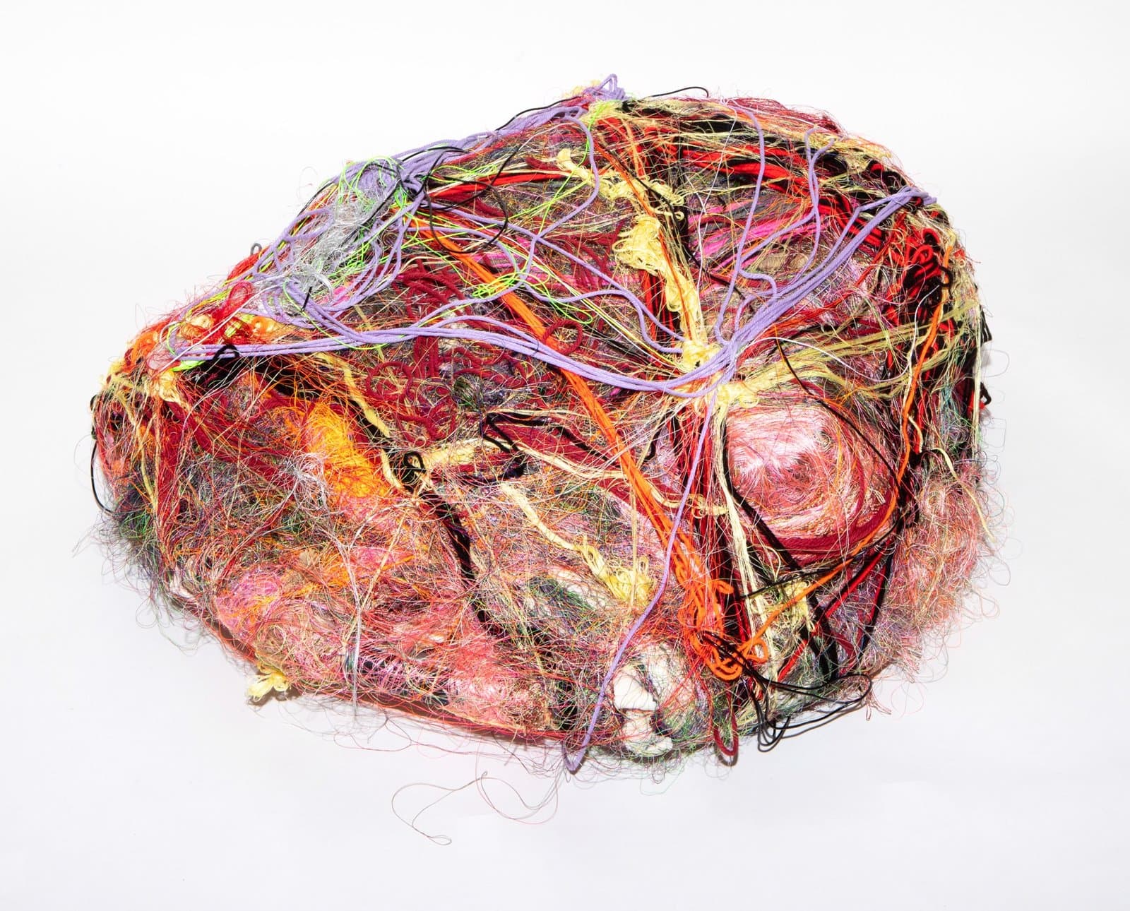 Mixed media sculpture of densely wrapped and tangled colorful threads, ribbons, and fibers in red, purple, yellow, and orange