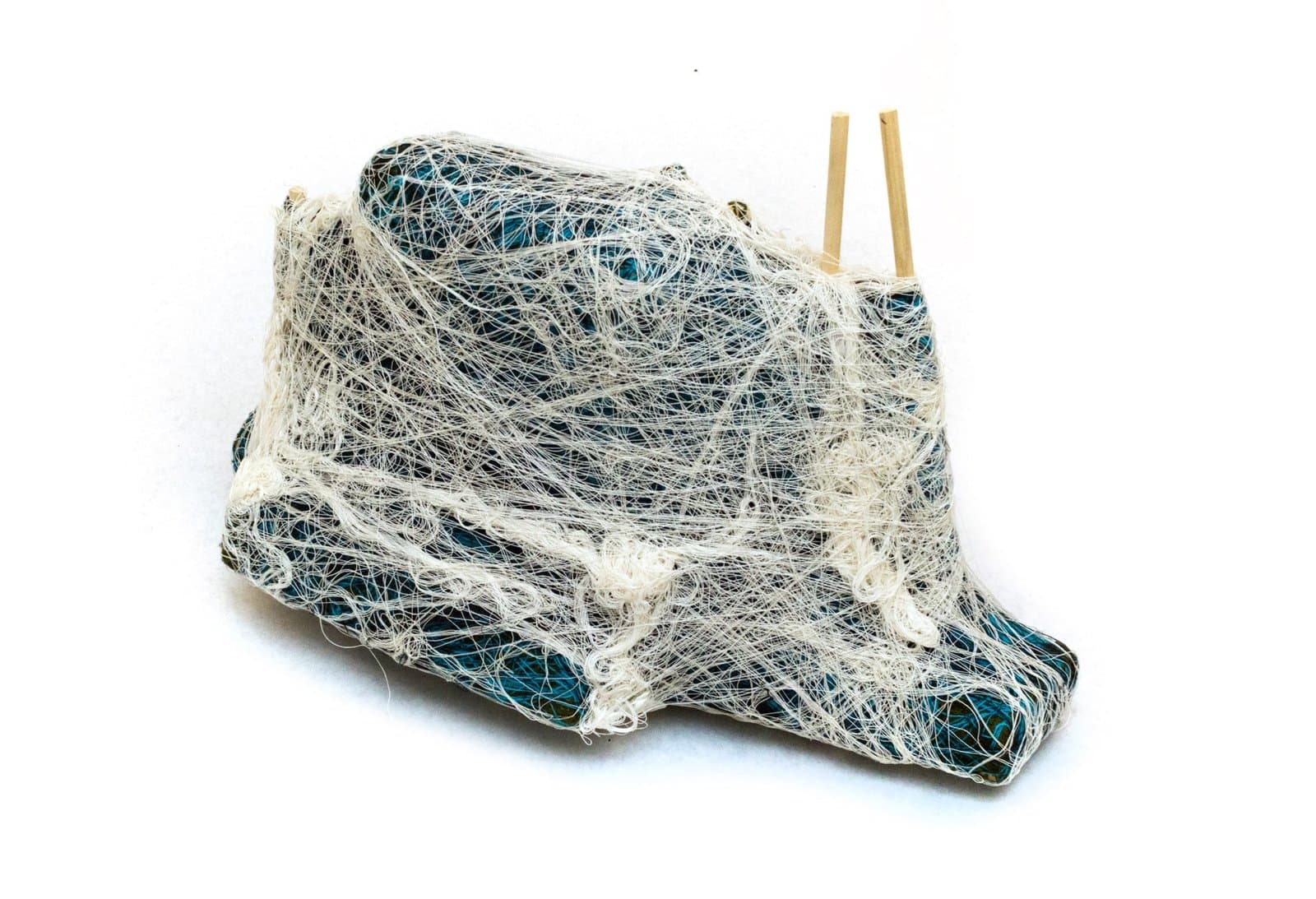 Fiber sculpture of bundled blue objects wrapped in white netting with wooden handles protruding