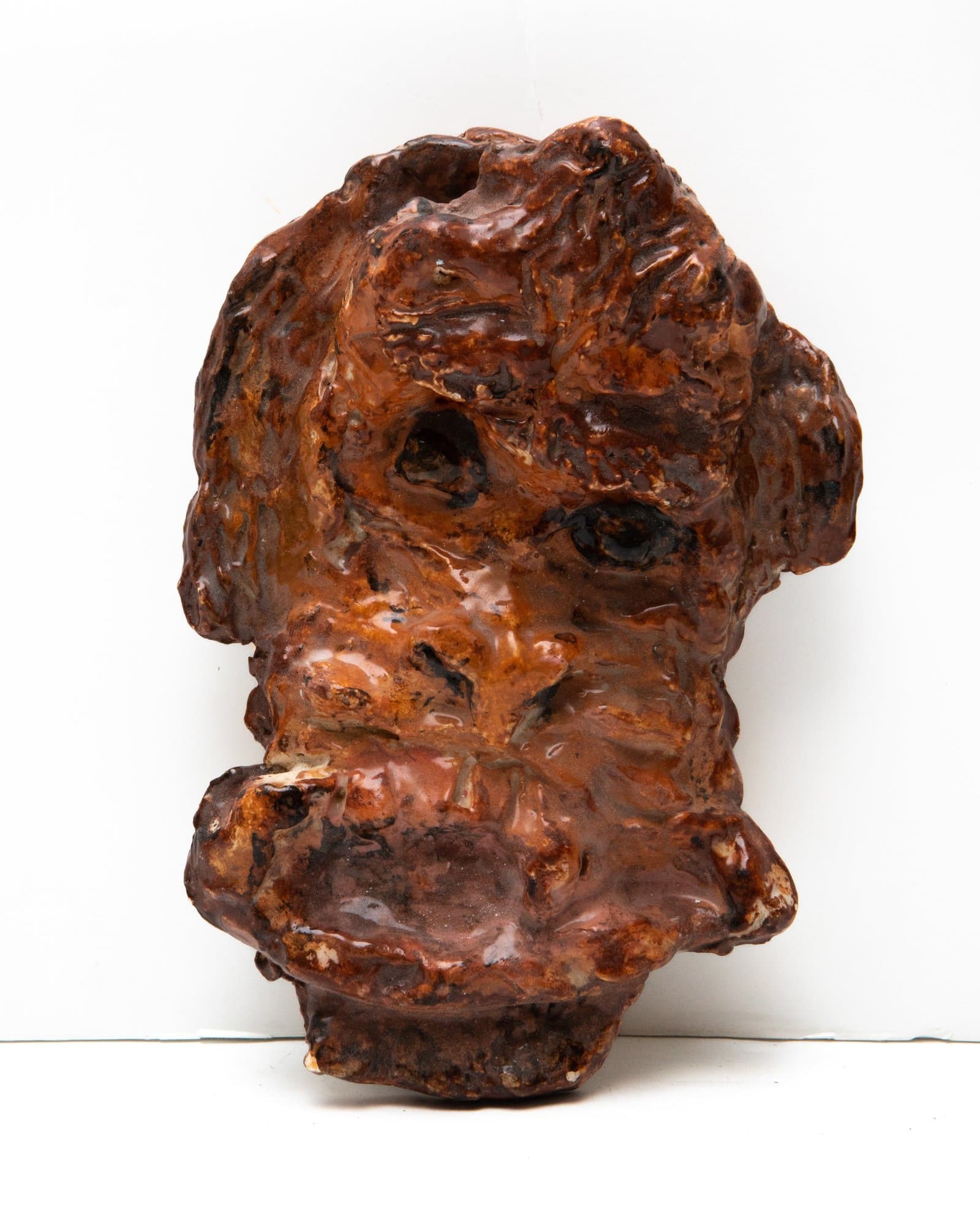 Glazed ceramic wall sculpture depicting a monkey face with deeply textured, irregular surface in warm reddish-brown tones.