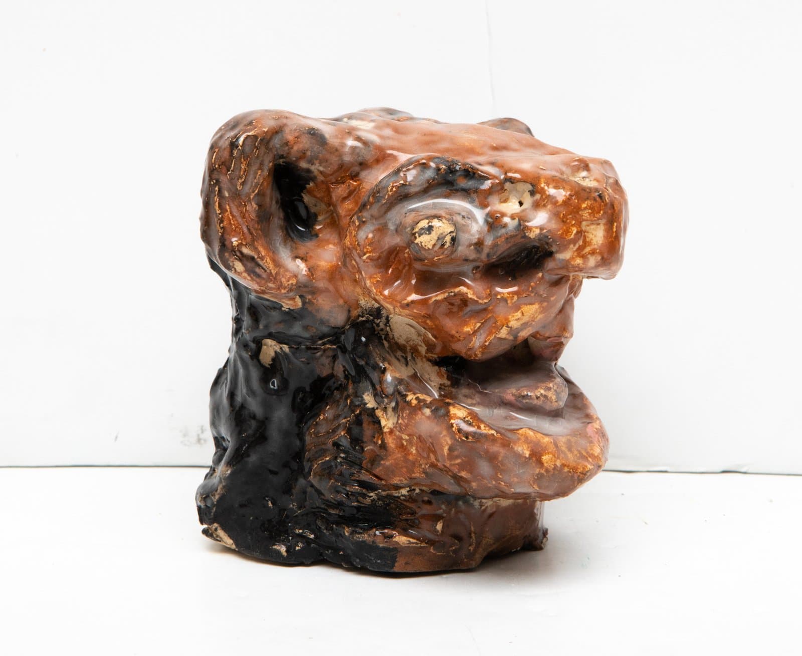 Glazed ceramic sculpture suggesting a face with bulbous forms in amber, black, and gold tones.