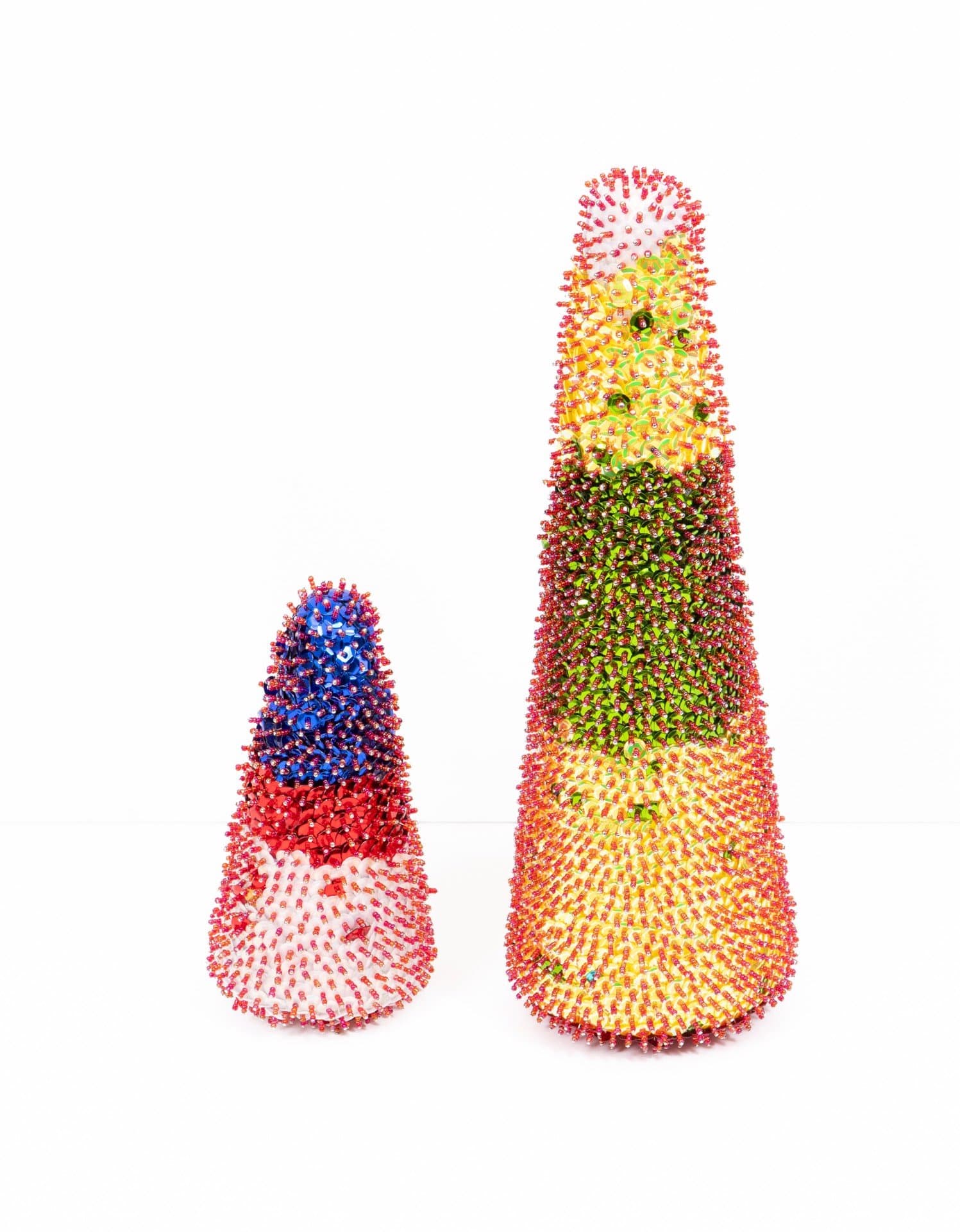 Two cone-shaped sculptures covered in multicolored sequins, one small and one large, on white background.