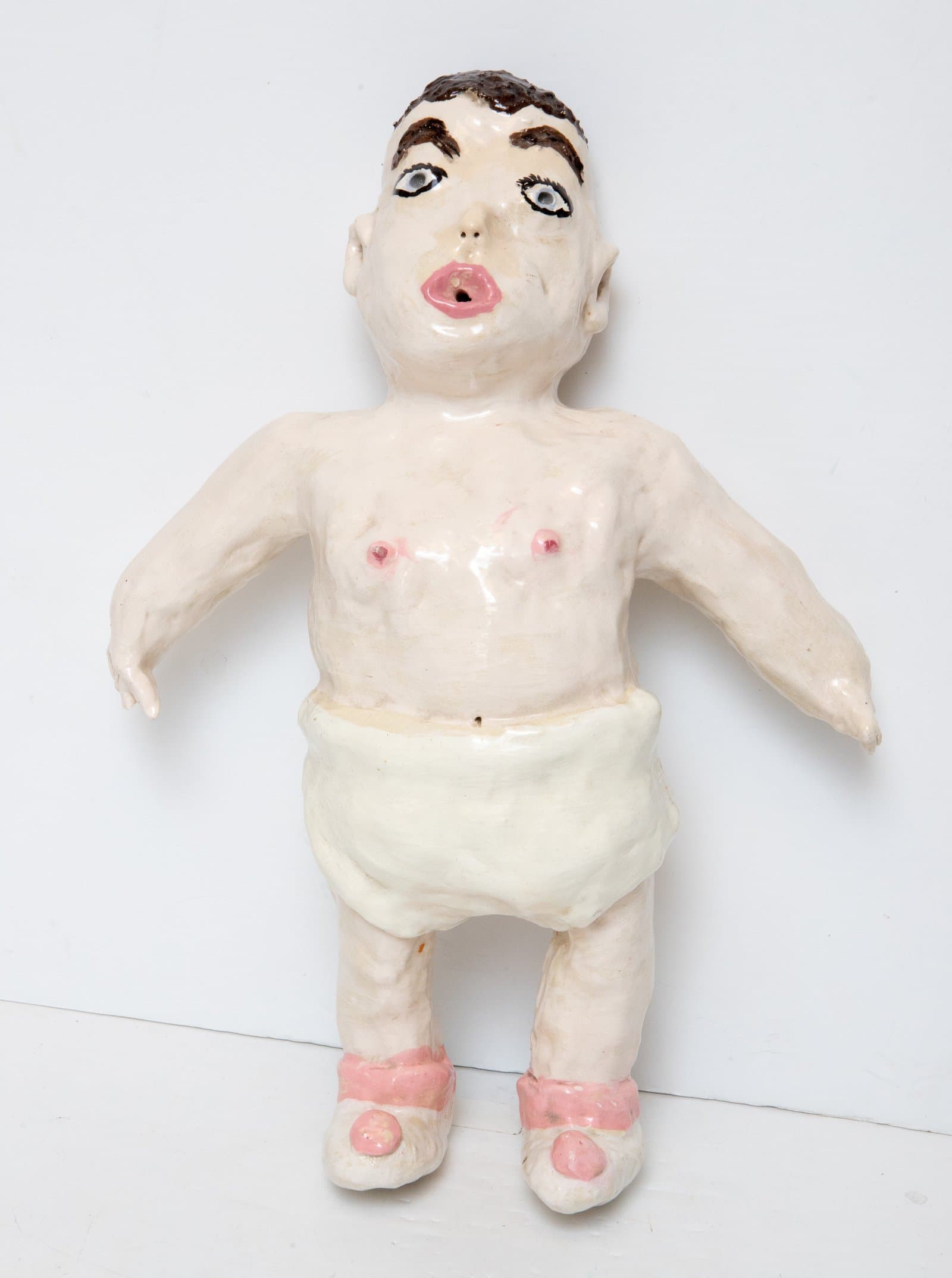 Ceramic figurine of a standing human figure with brown hair, white glaze, pink accents, wearing a diaper and pink shoes.