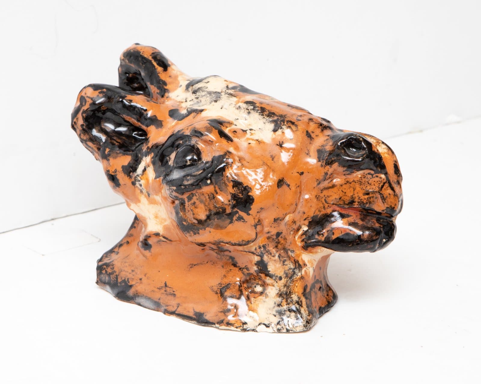 Glazed ceramic sculpture of an animal head, likely a horse or cow, in orange and black on a white surface.