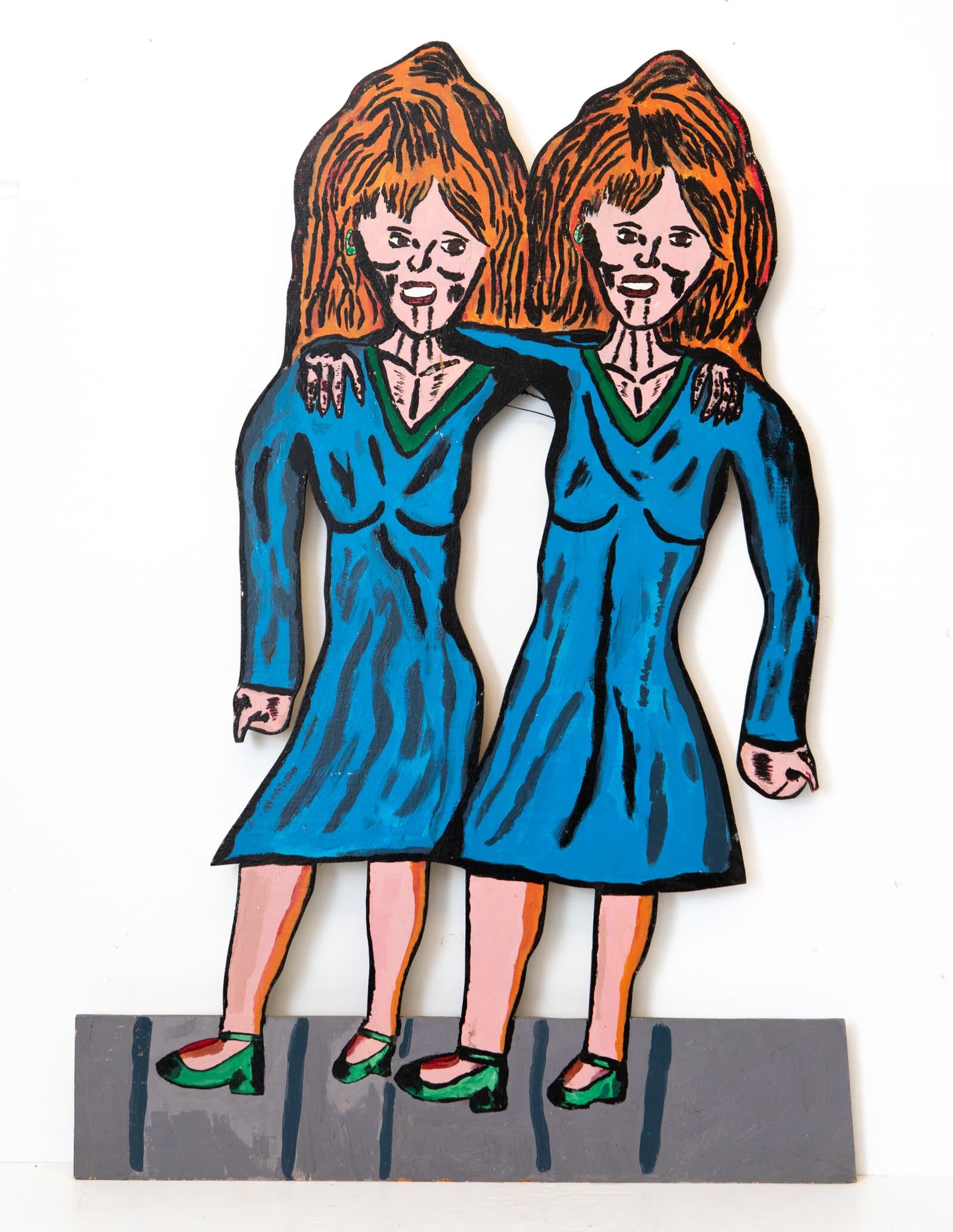 Painted wood cutout sculpture of two women with auburn hair in matching blue dresses with arms around each other.