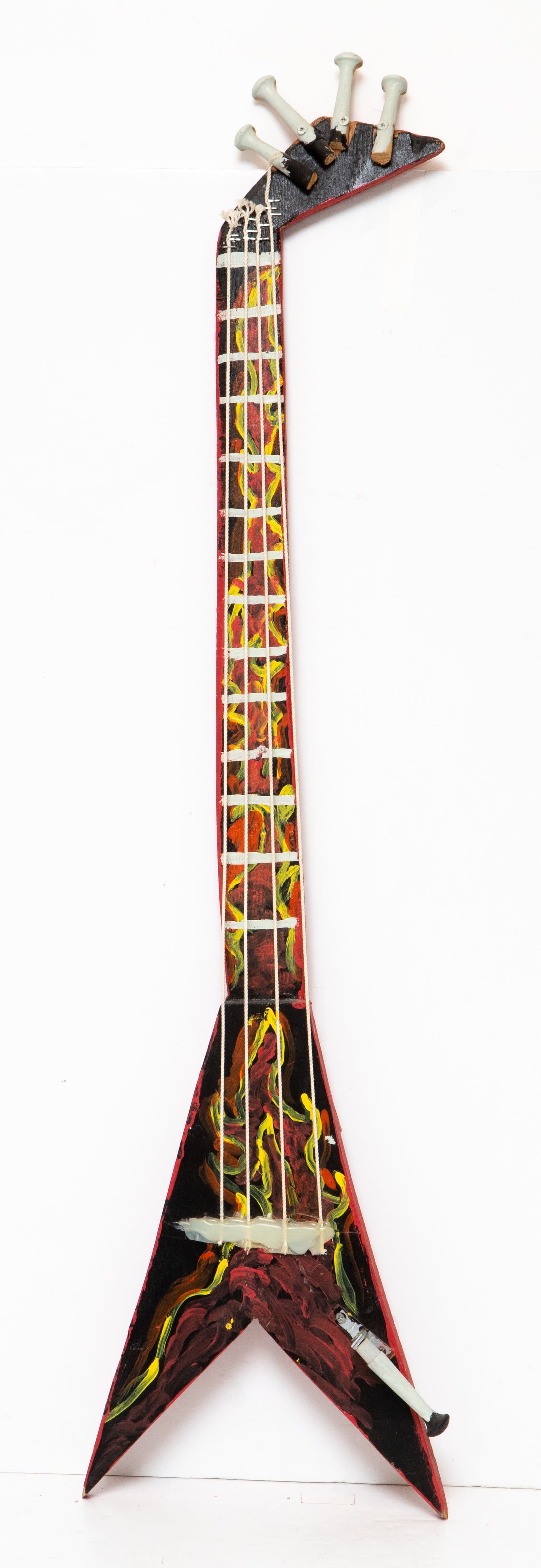 Painted wood guitar sculpture with V-shaped body, decorated with flame-like brushstrokes in red, yellow, and black.