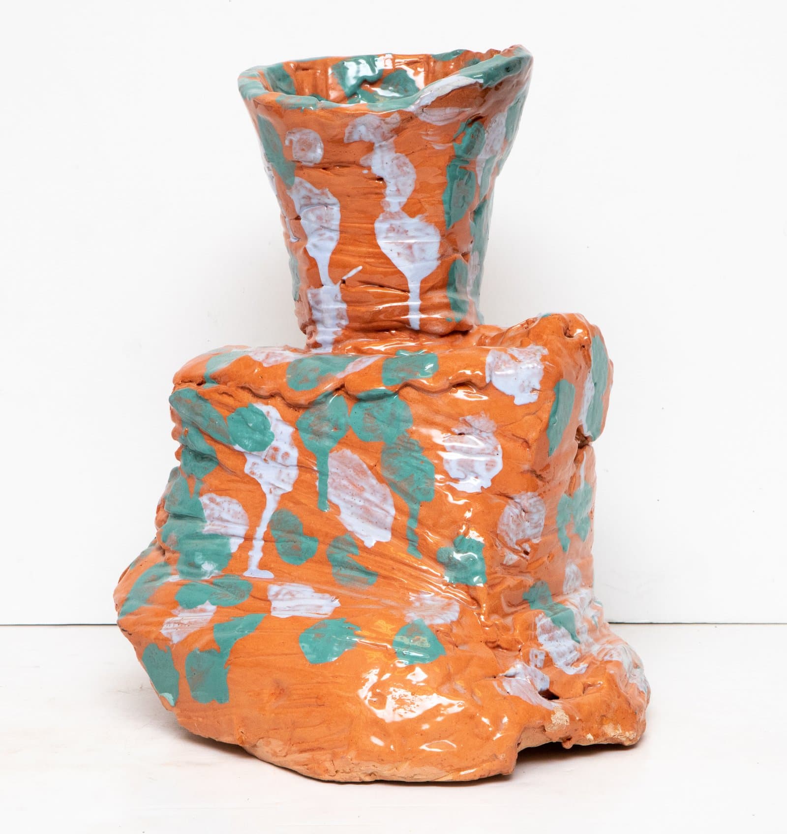 Glazed ceramic vessel with irregular blocky base and flared neck opening, covered in orange, teal, and white glaze.