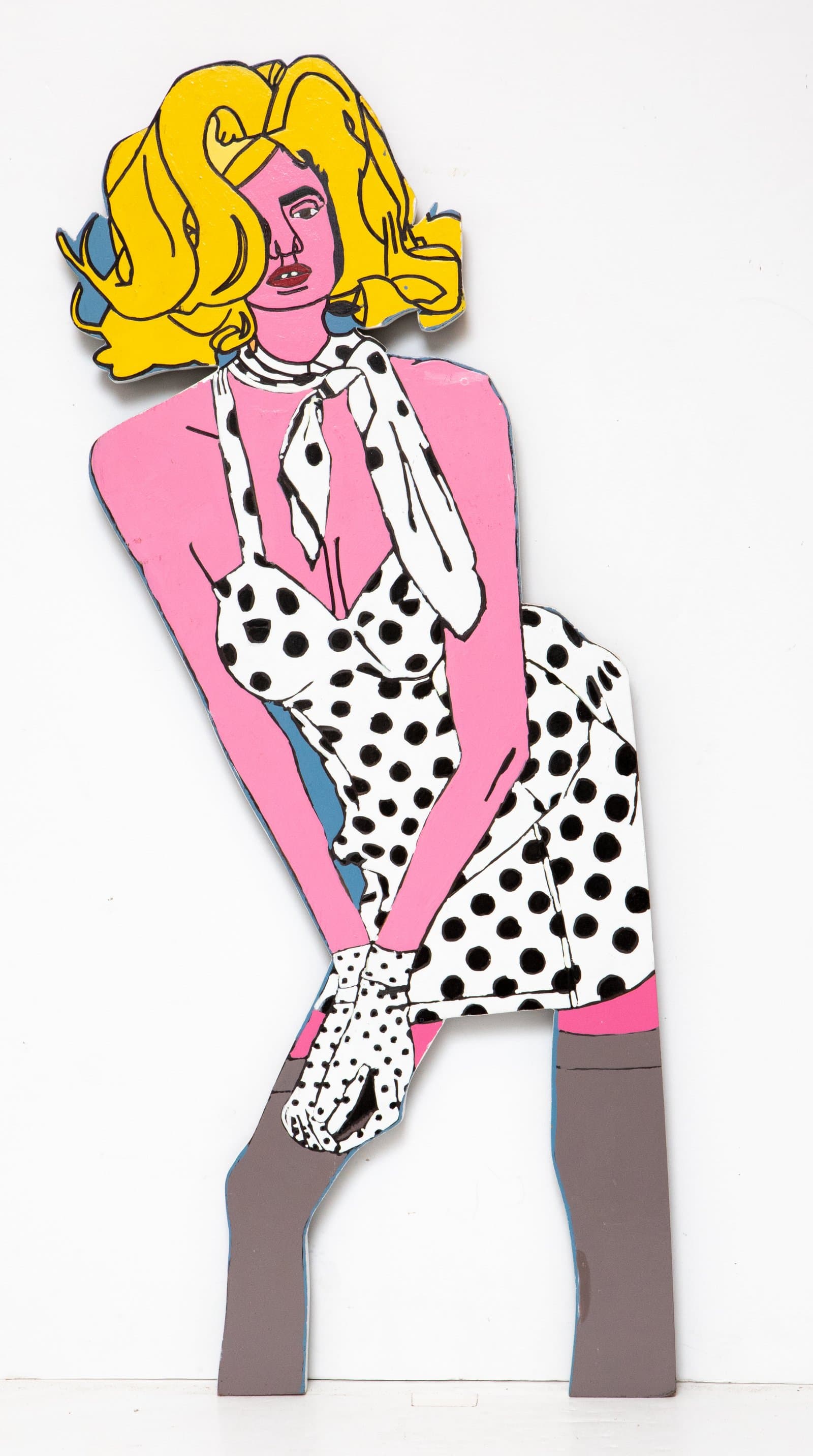 Cutout wood sculpture of a seated woman with yellow hair, pink skin, black-and-white polka dot dress, and gray boots, painted in acrylic.