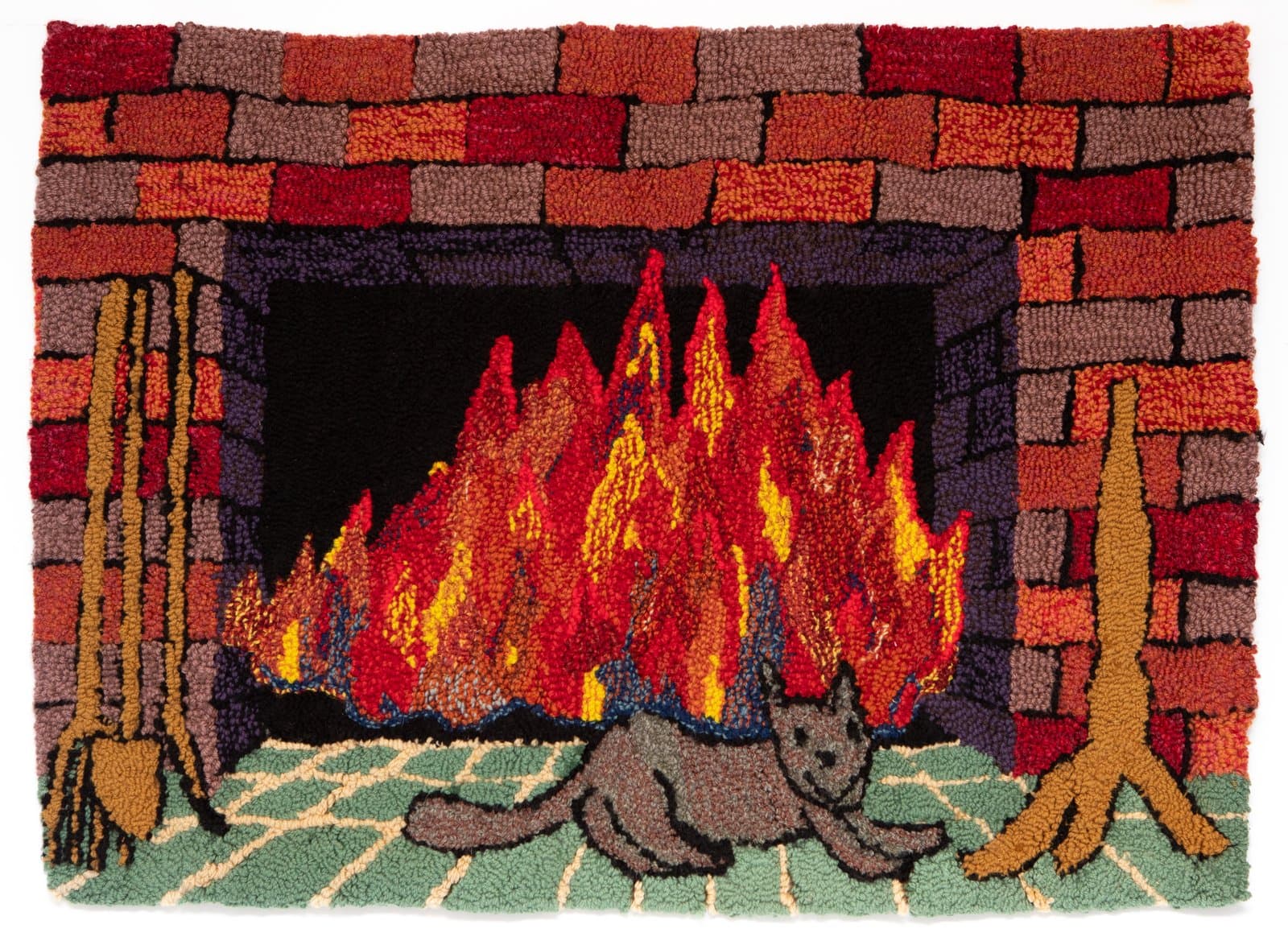 Hooked rug depicting a cat resting before a roaring fireplace framed by brick, with brooms on each side.