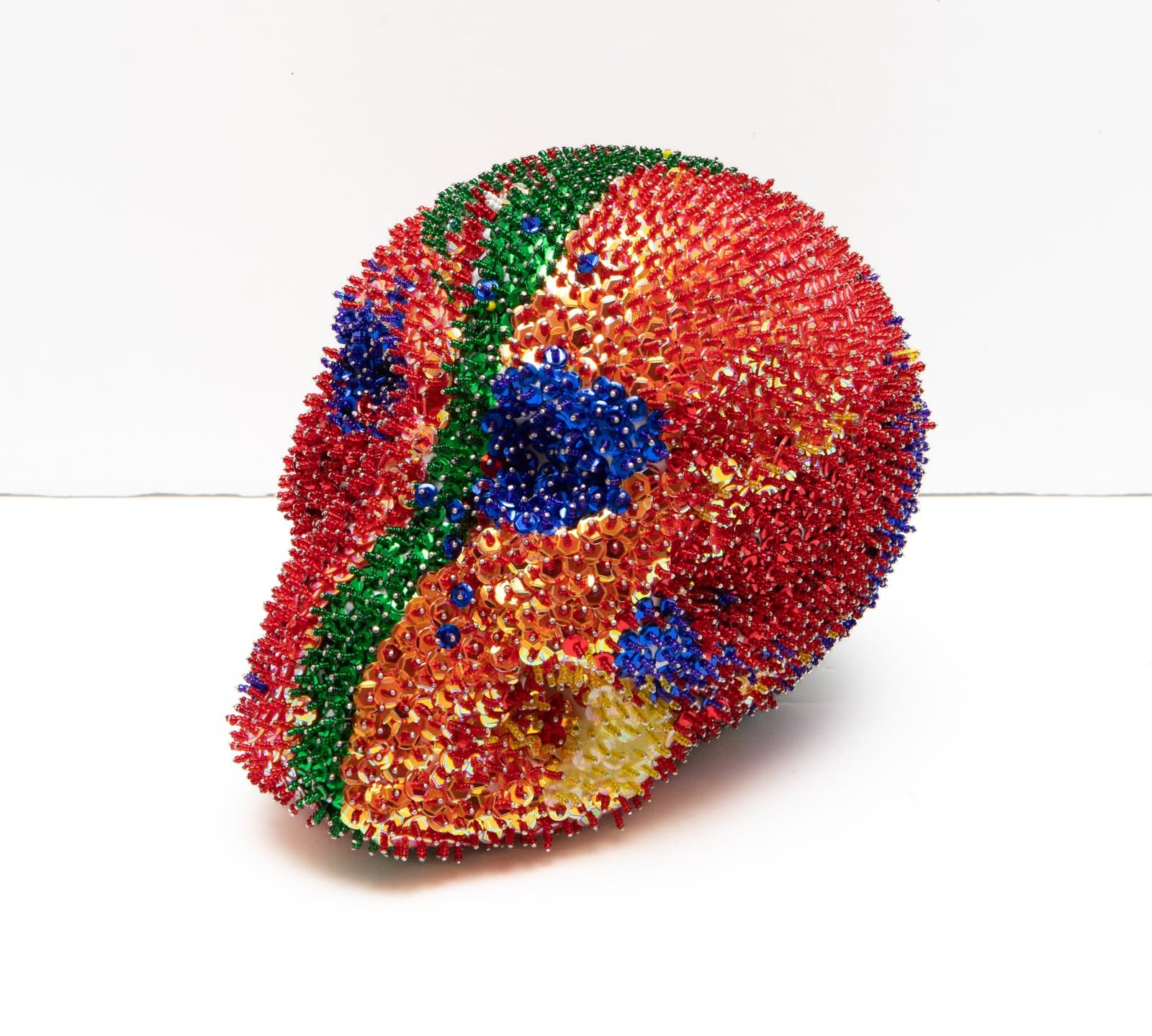 Skull-shaped sculpture densely covered in multicolored sequins and beads in red, blue, green, orange, and yellow.