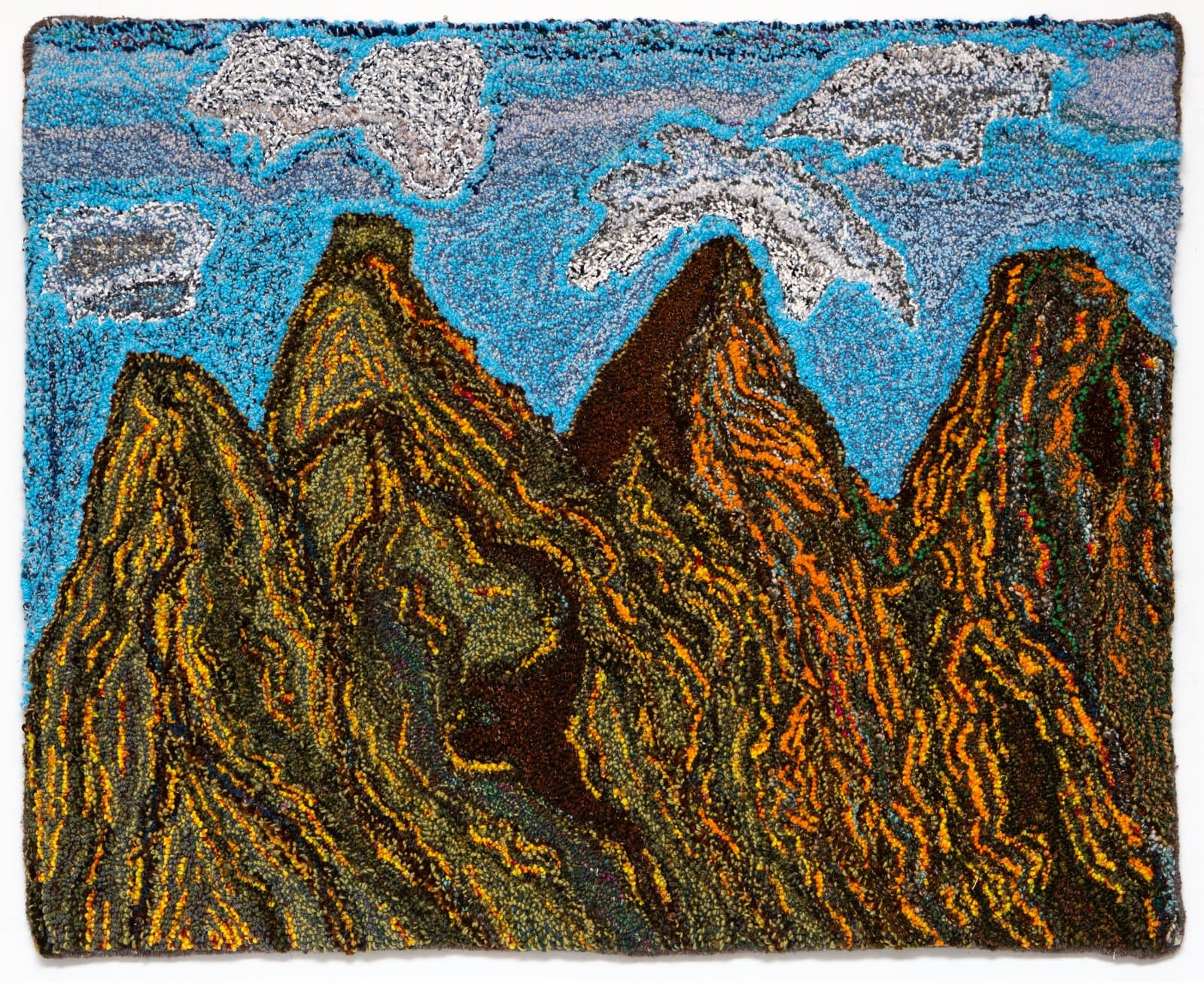 Hooked rug depicting jagged mountain peaks in orange, brown, and green beneath a blue sky with white clouds.