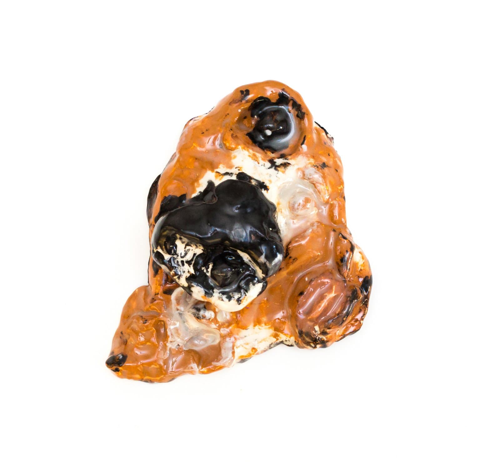 Small ceramic sculpture with lumpy, irregular form glazed in amber orange, glossy black, and cream white.