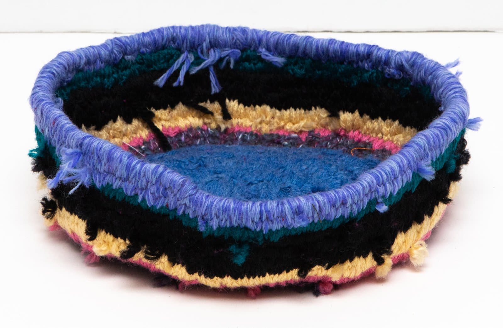 Handmade yarn basket with horizontal stripes in black, yellow, teal, pink, and blue; blue yarn rim with fringe details.