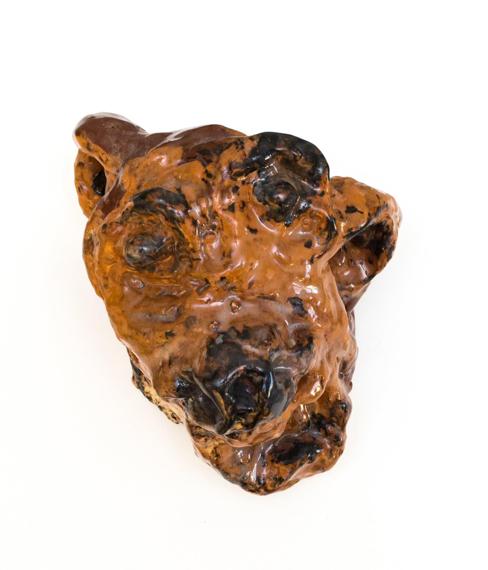 Glazed ceramic sculpture of an animal head, roughly modeled, with amber-brown and dark black mottled glaze.