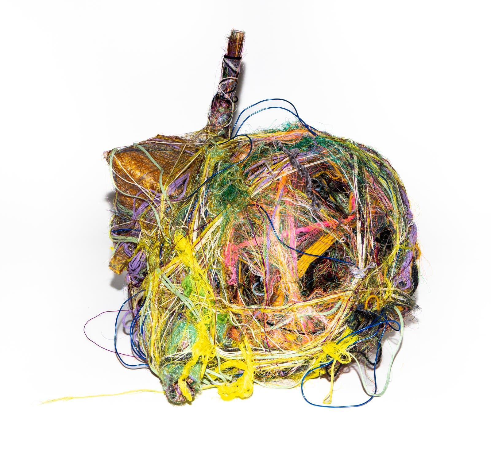 Spherical wrapped sculpture of densely tangled multicolored fibers and threads around a dark core, with a stick protruding from the top.