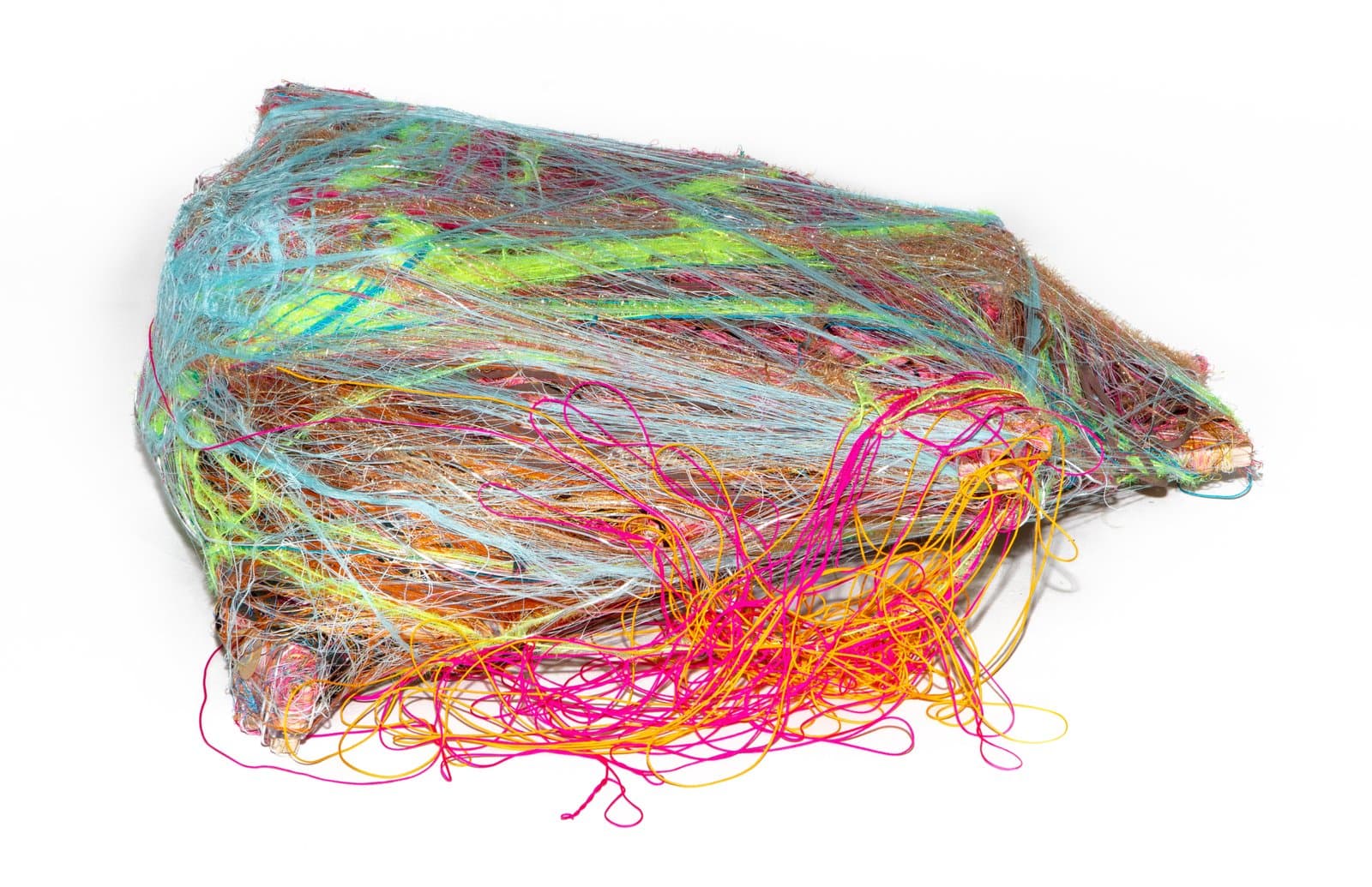 Textile sculpture made of densely layered multicolored threads and fibers forming a compact, irregular mound shape.