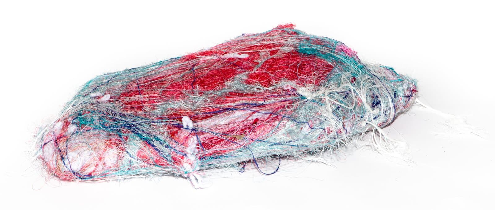 Wrapped sculpture made of tangled multicolored threads and fibers in red, teal, white, and navy, forming an oval mound.