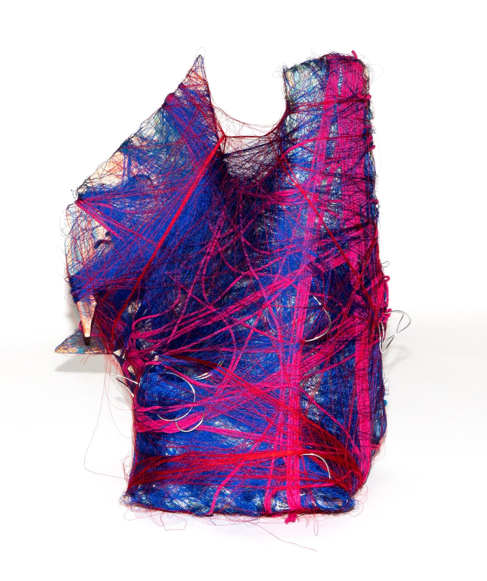 Abstract fiber sculpture wrapped in vivid magenta and blue yarn with metal safety pins, roughly vessel-shaped, on white background.