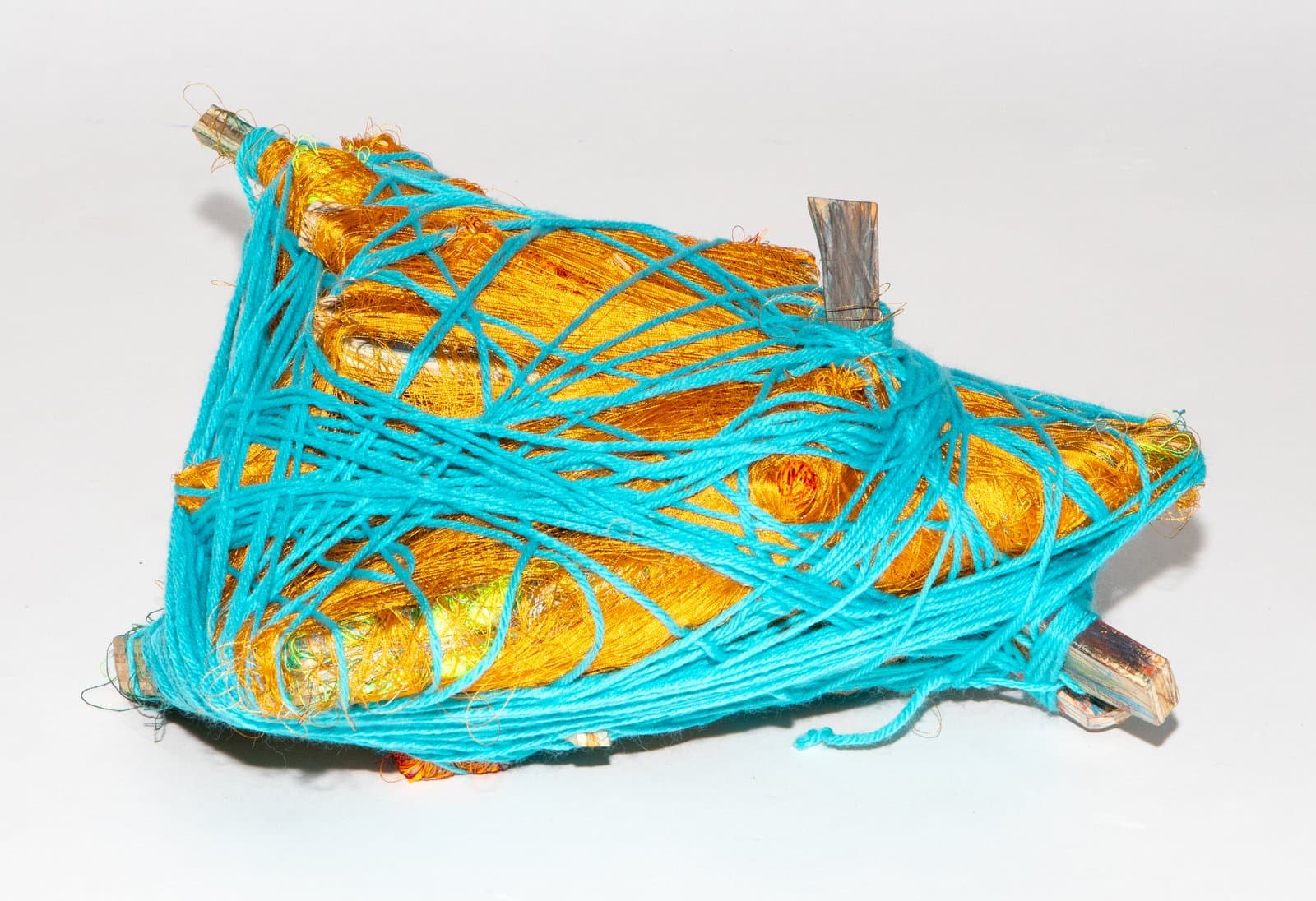 Small triangular fiber sculpture wrapped in turquoise yarn over a gold metallic base with protruding wooden sticks.