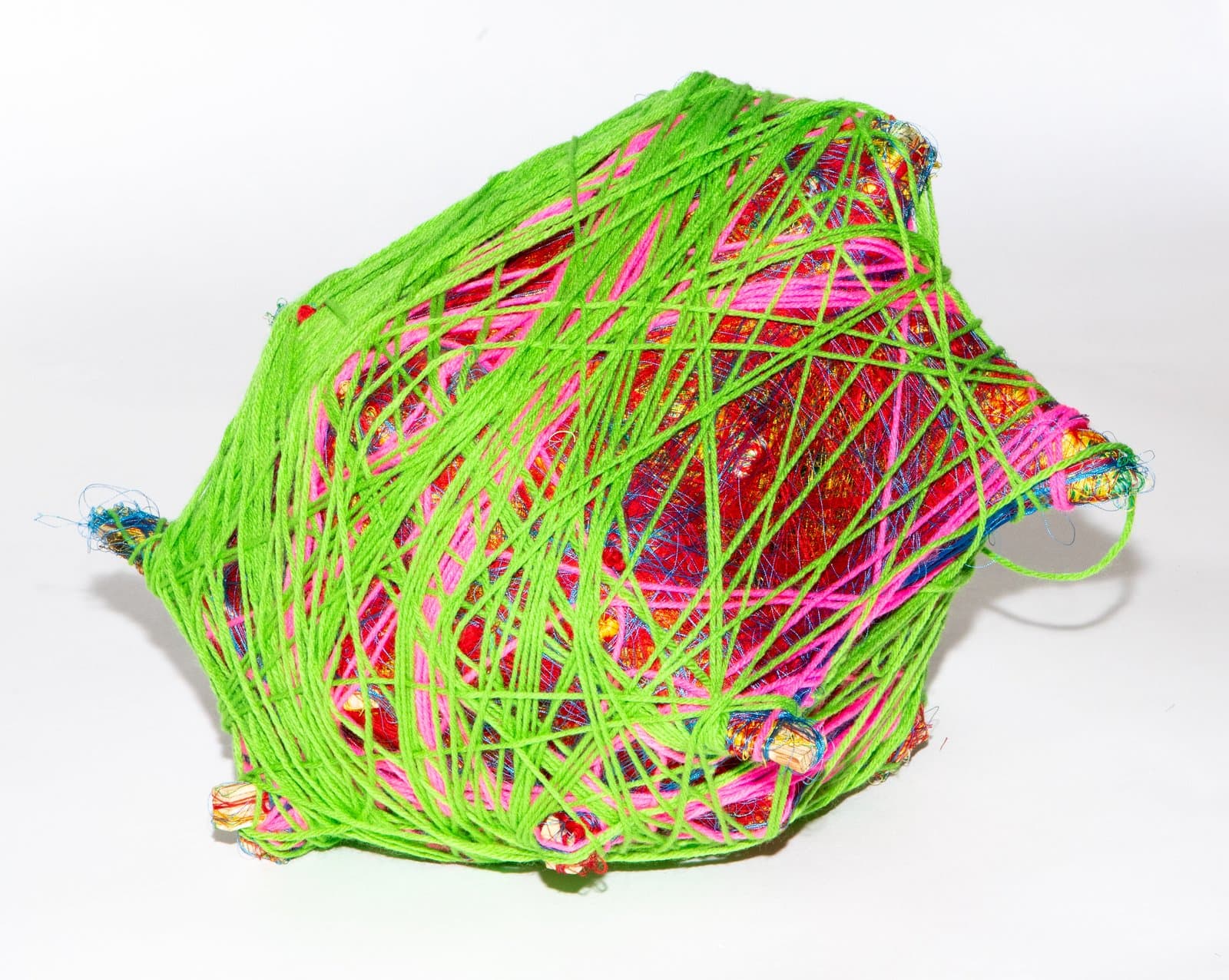 Wrapped fiber sculpture with neon green yarn crisscrossed over a multicolored textile base in pink, red, and gold.
