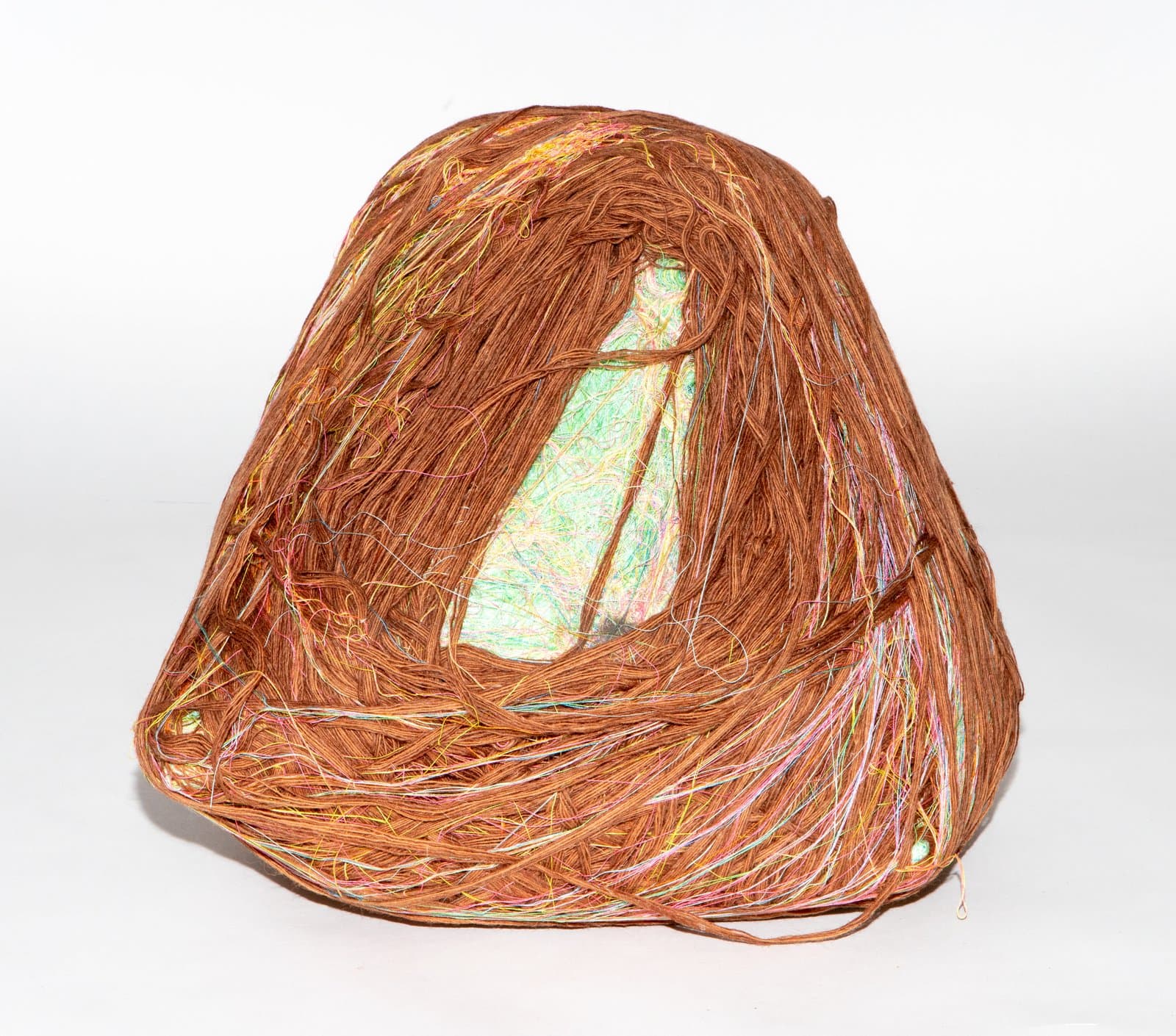 Dome-shaped fiber sculpture wrapped densely in rust-brown yarn with multicolored strands, revealing a hollow interior with iridescent lining.