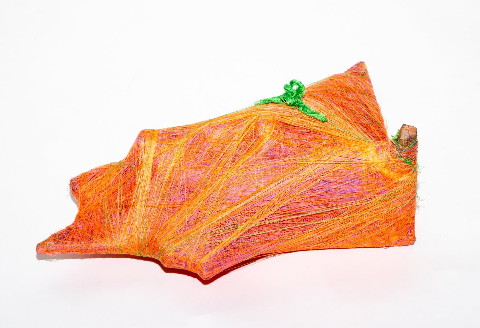 Abstract wrapped fiber sculpture in orange, yellow, and pink with green yarn accent, angular irregular form on white background.