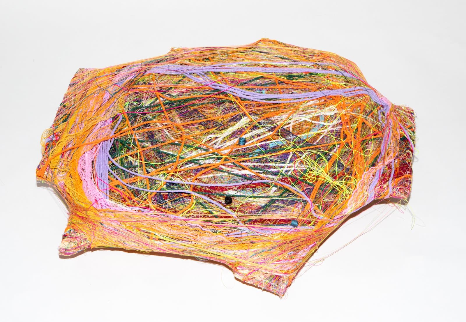 Oval wrapped sculpture densely layered with multicolored threads and fibers in orange, pink, yellow, green, and lavender.