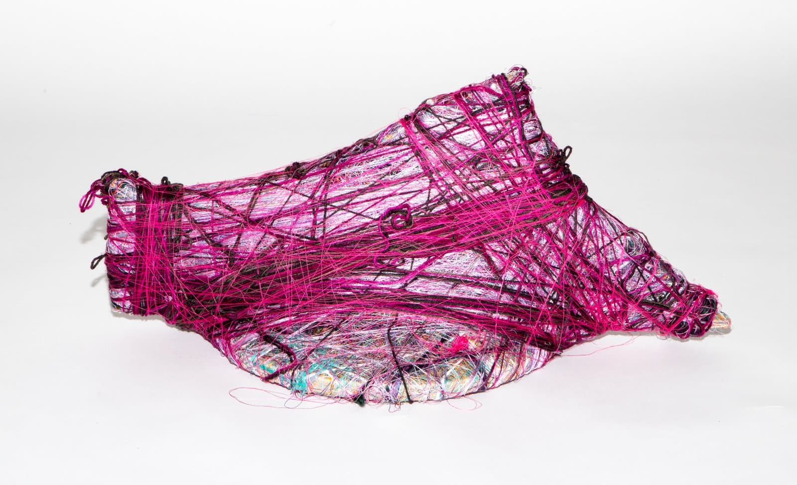 Sculptural form wrapped densely in magenta and dark thread over a multicolored base, roughly shoe-shaped, on white background.