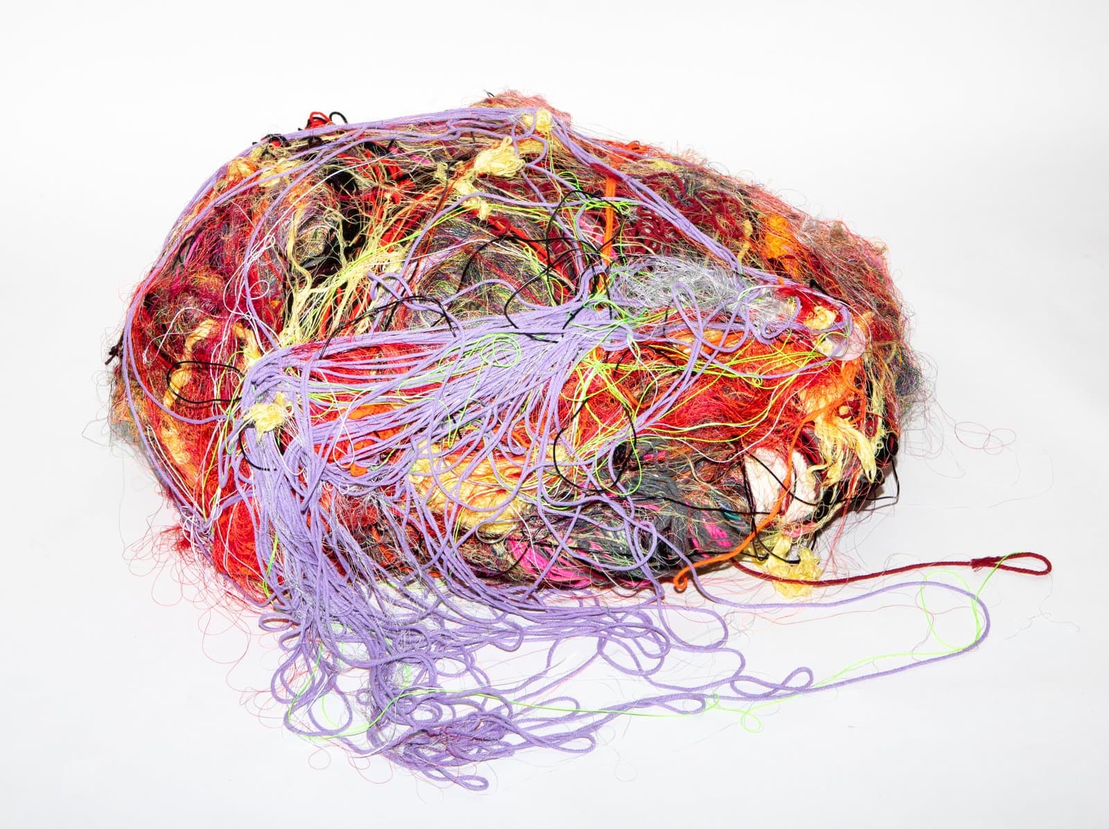 Oval wrapped fiber sculpture with dense multicolored yarn in red, orange, yellow, and lavender on white background.