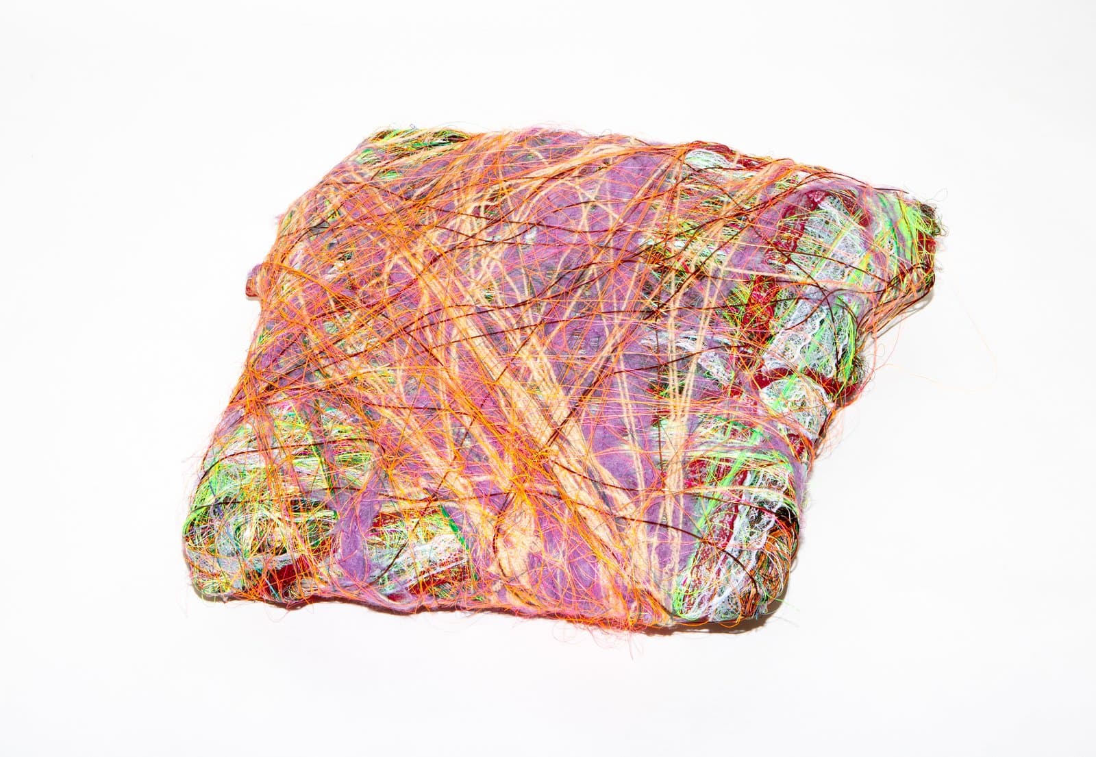 Roughly square wrapped textile sculpture with layered fiber strands in orange, green, pink, and purple on white background.