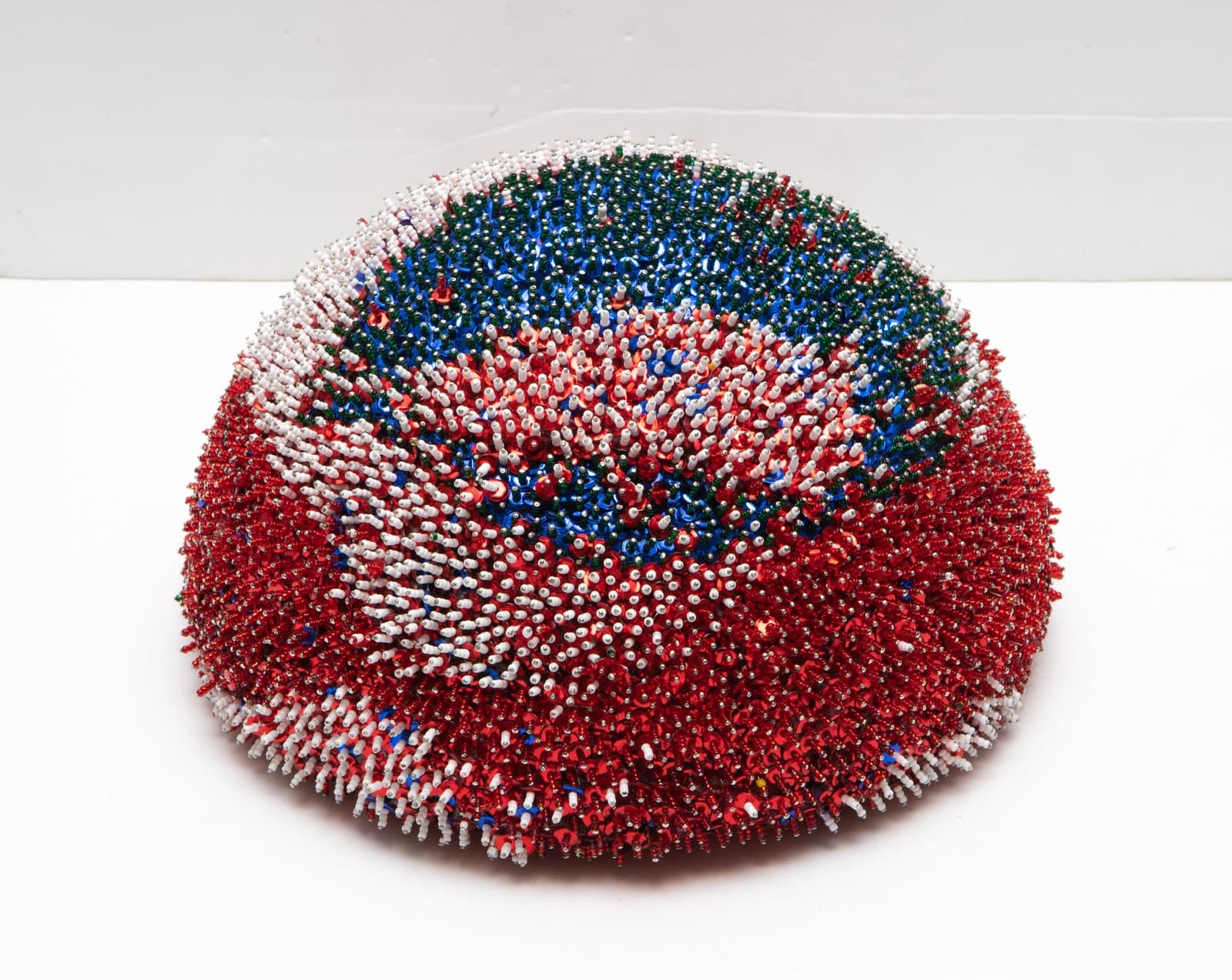 Dome-shaped sequin sculpture covered in densely packed red, white, blue, and green sequins forming swirling patterns.