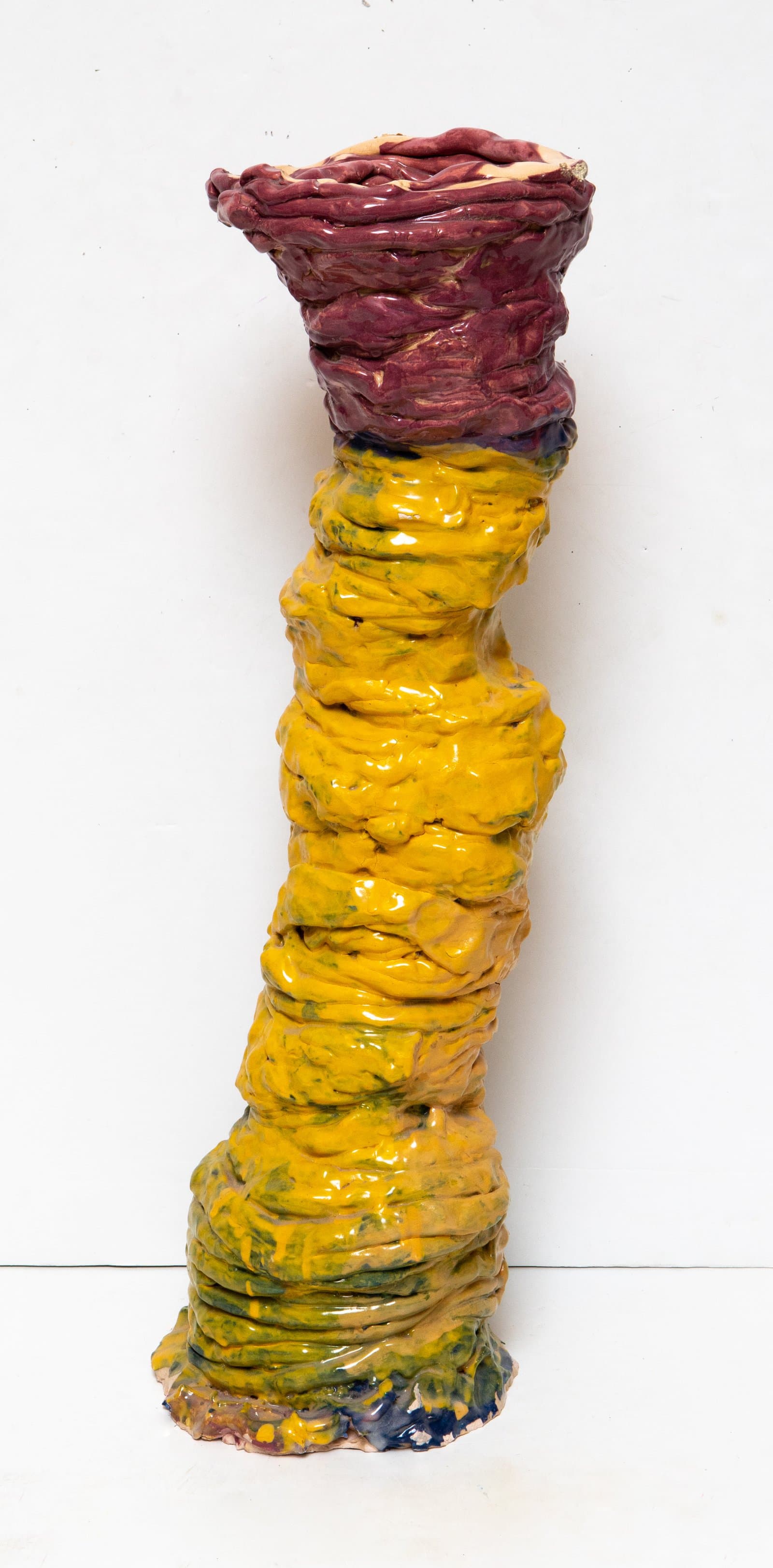 Tall ceramic column sculpture with coiled, ridged texture; bright yellow-green lower body and deep burgundy upper section.