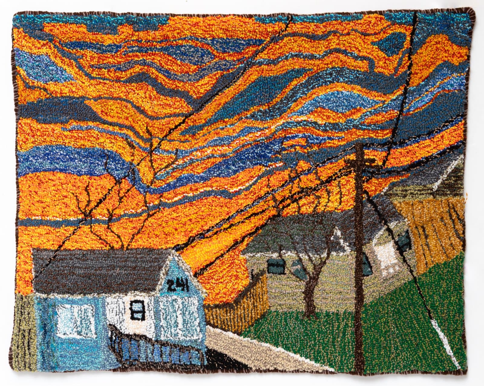 Hooked rug depicting a neighborhood street scene beneath a dramatic swirling orange and blue sunset sky.