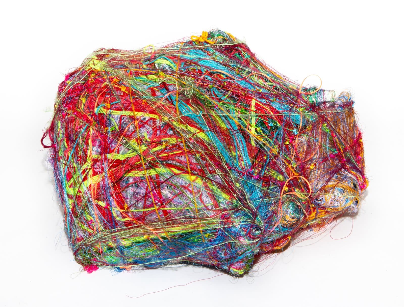 Dense wrap sculpture of tangled multicolored threads and fibers forming an irregular mound on a white background.