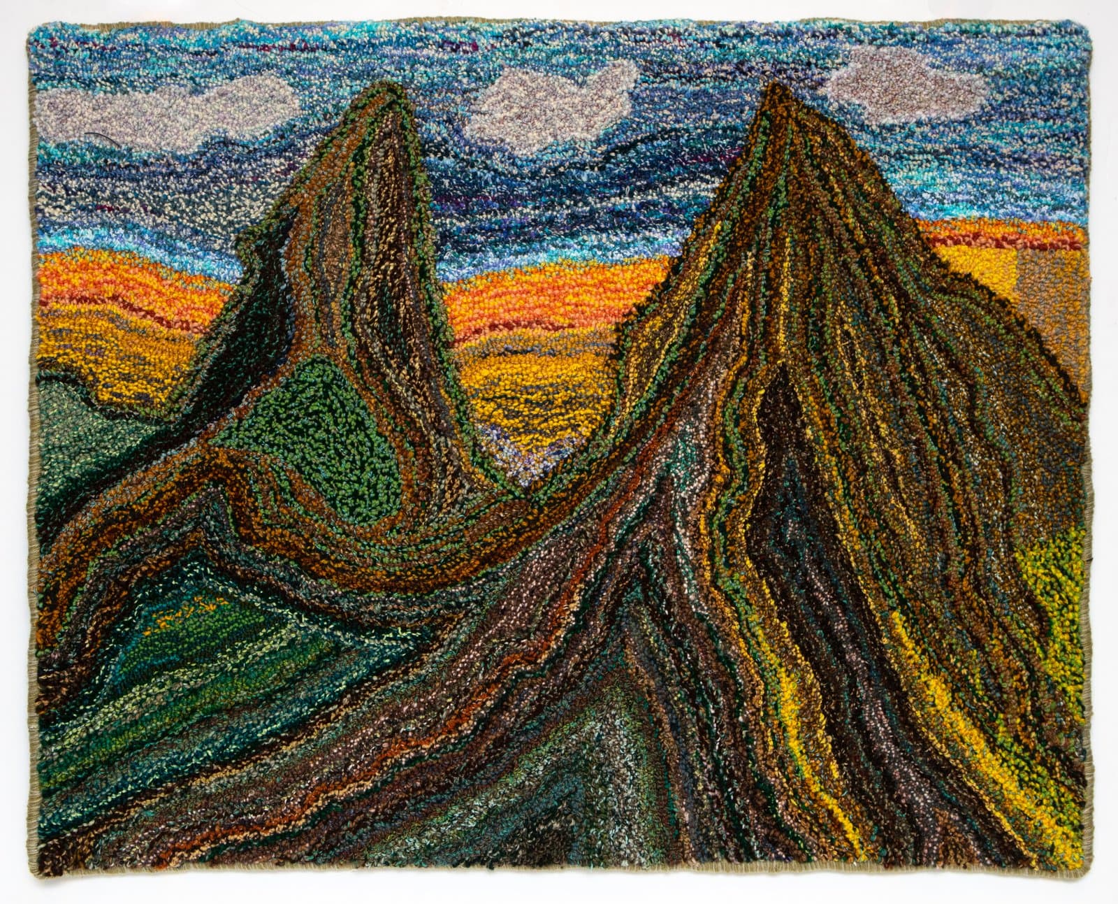 Hooked textile depicting two jagged mountain peaks in browns and greens beneath a blue sky with clouds and orange horizon.