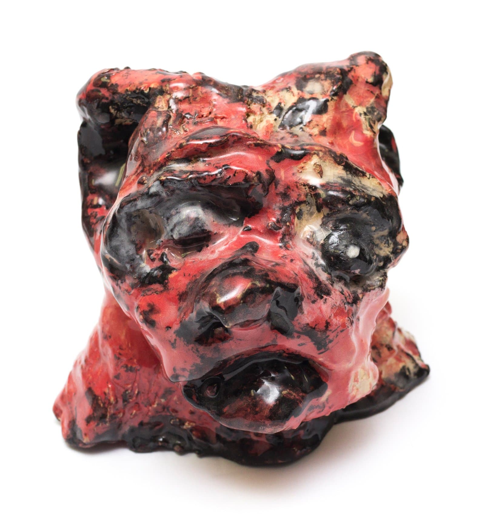 Ceramic sculpture of a cat-like head with pointed ears, glazed in red and black with rough, uneven texture.