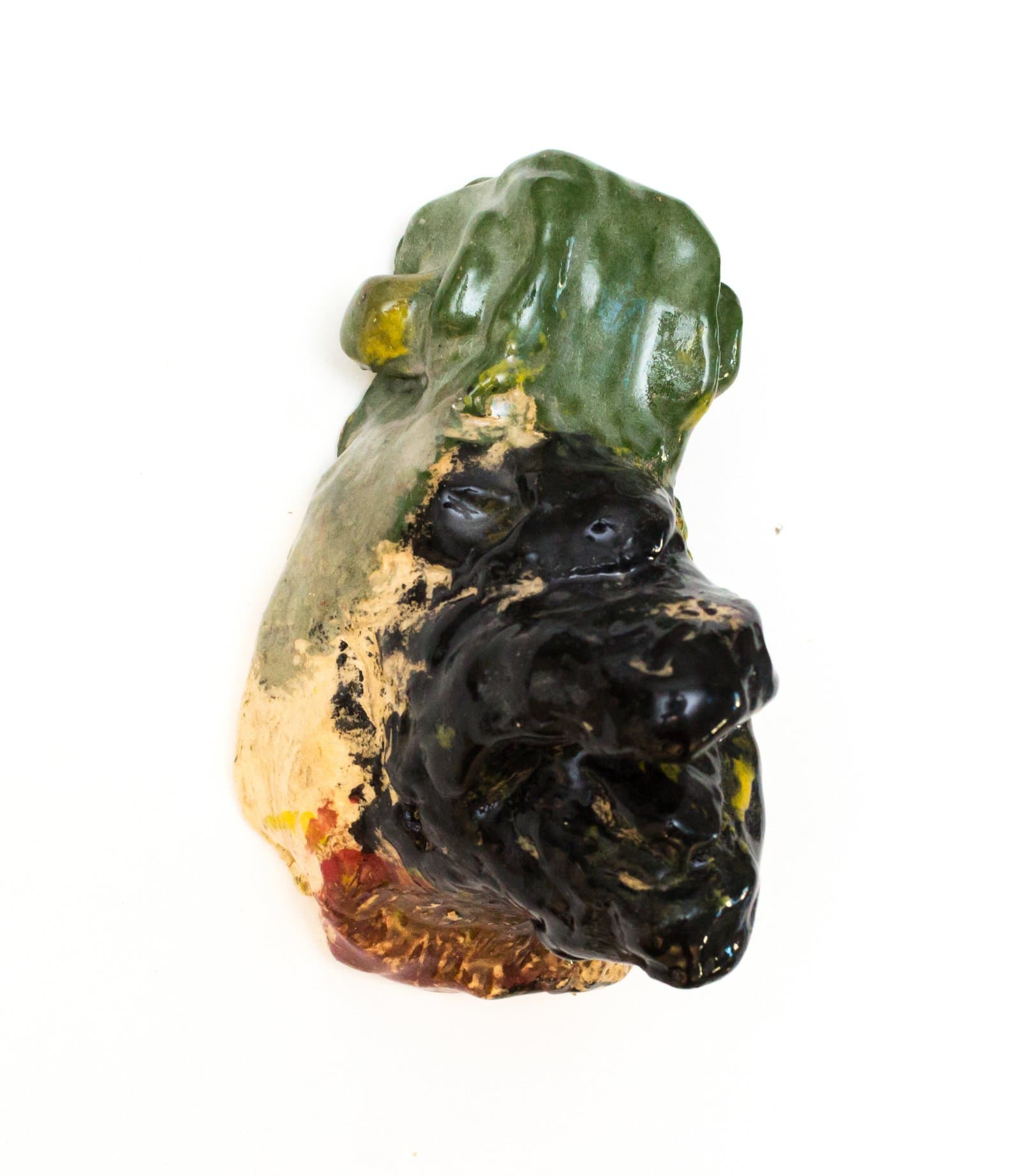 Glazed ceramic wall sculpture depicting an animal face in black glaze with green foliage forms above, on white background.