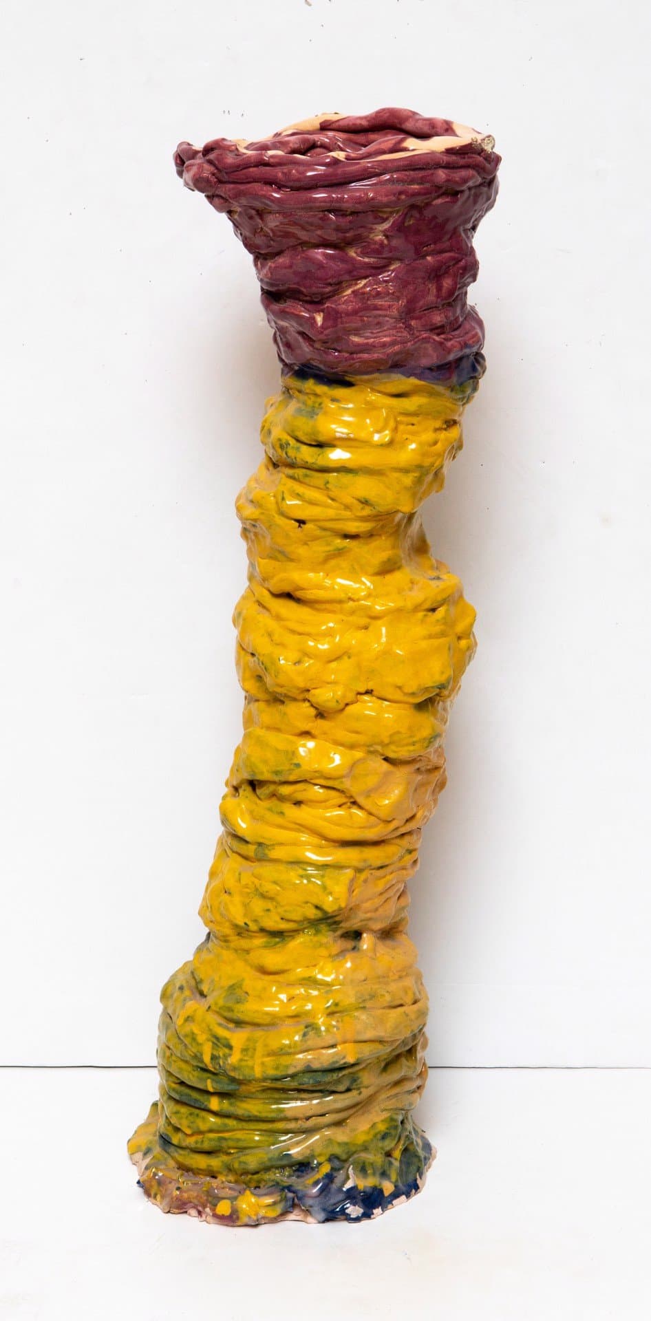 Vertical ceramic sculpture with coiled rope-like form in yellow and dark red glazes on white background.