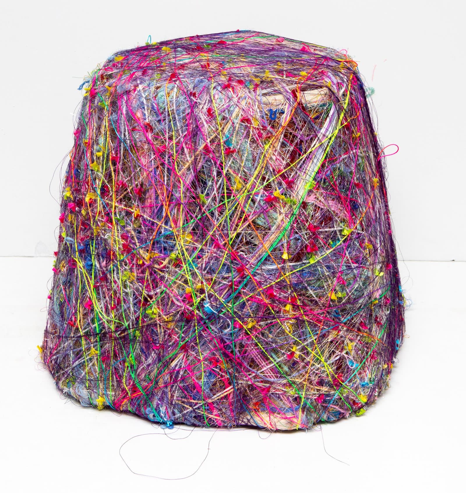 Rounded trapezoidal sculpture densely wrapped in multicolored thread and yarn with small knotted embellishments throughout.