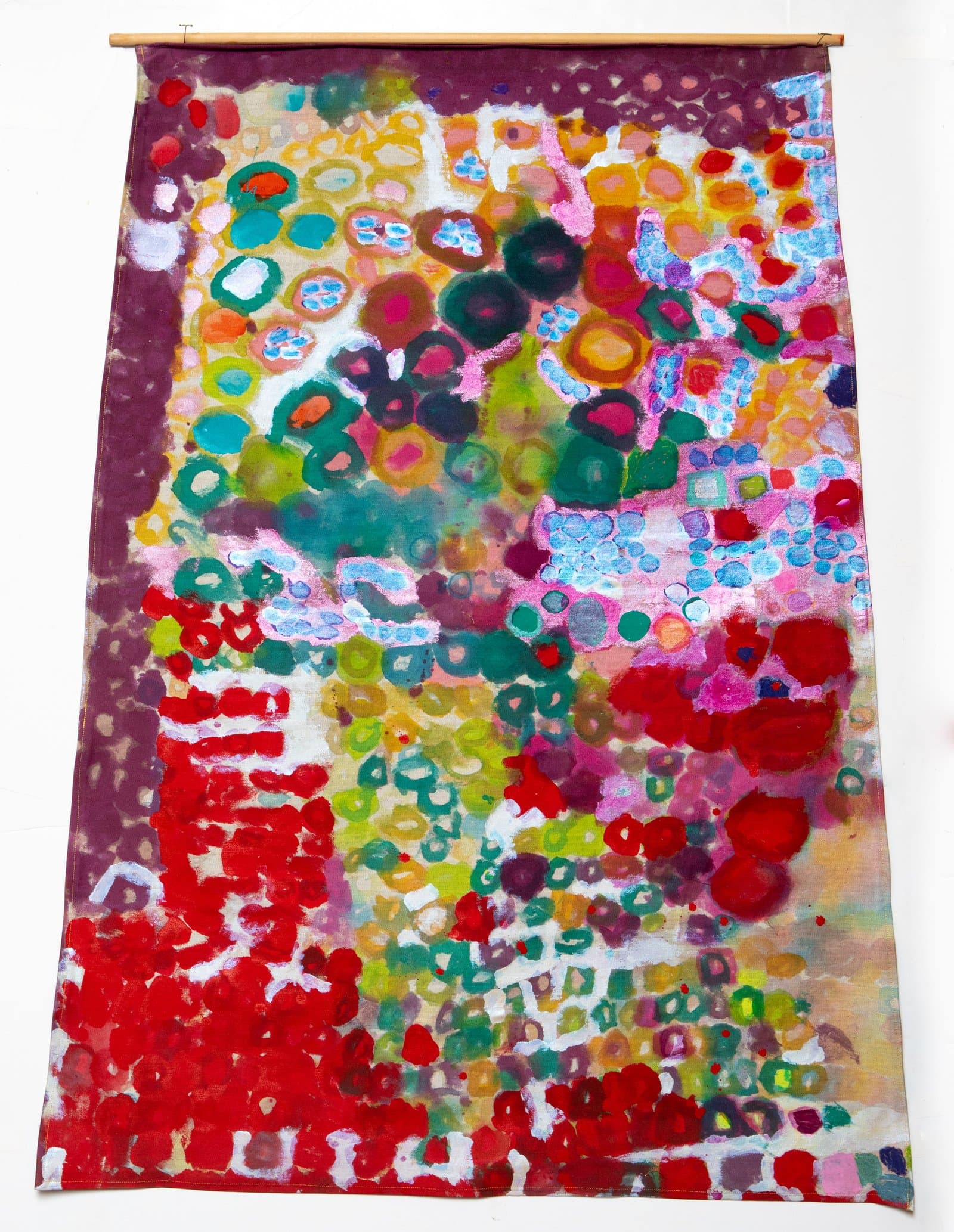 Large abstract acrylic painting on unstretched canvas hung from a wooden dowel, densely covered in multicolored oval and circular forms.