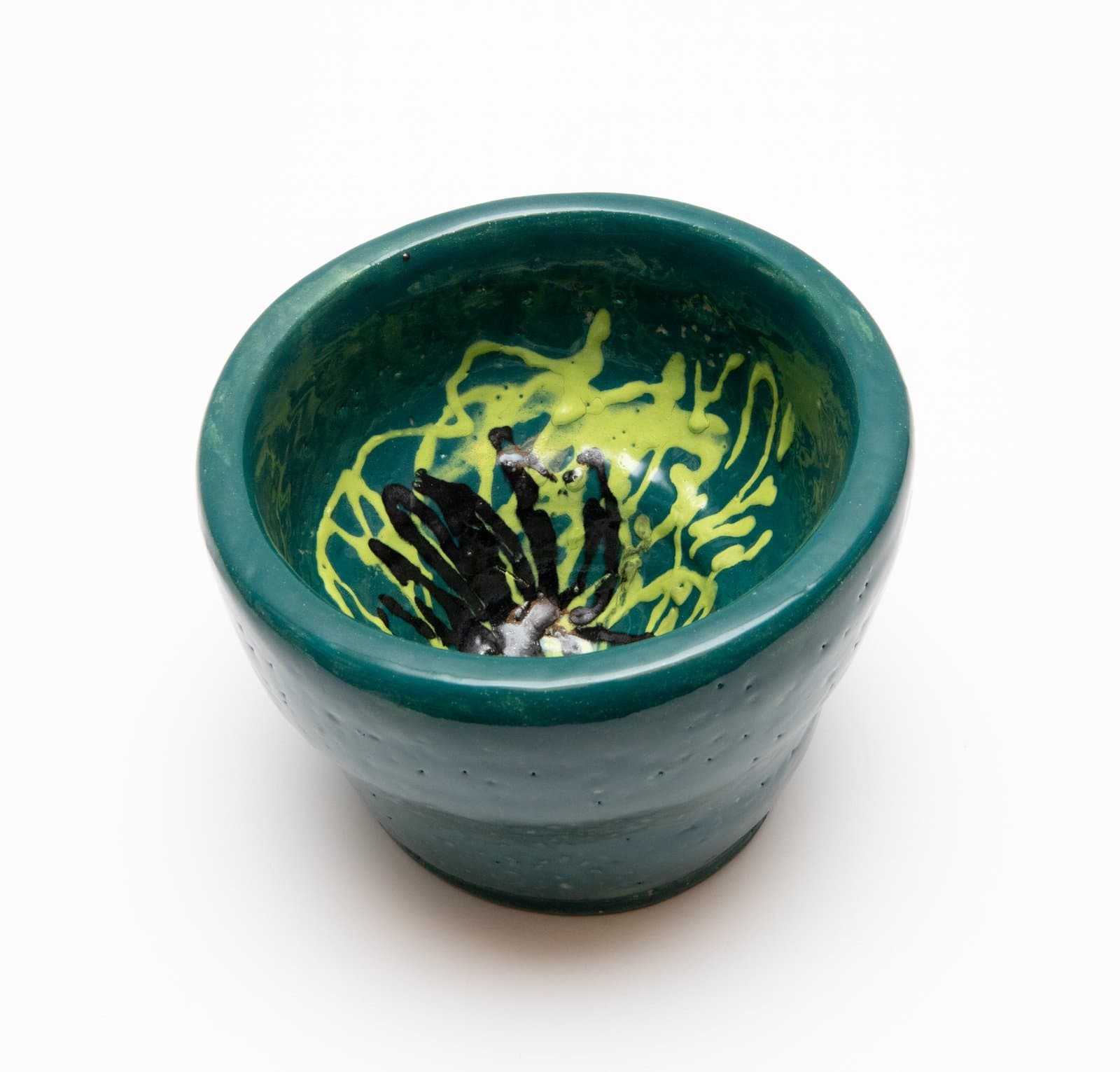 Small ceramic cup with teal glaze exterior and interior decorated with yellow-green drips and black brushwork.